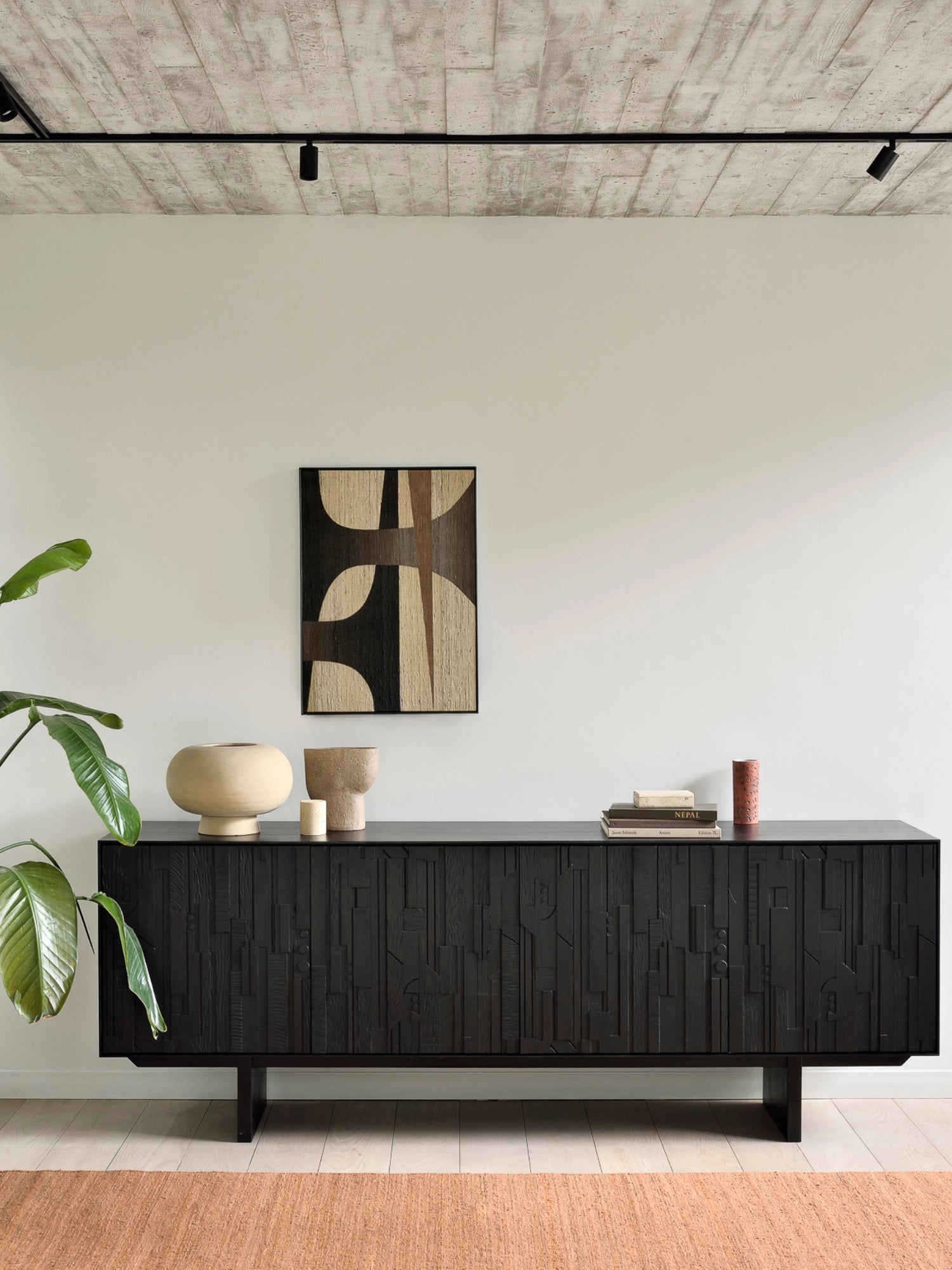 Ethnicraft Mosaic Sideboard in Teak Off-Black, a contemporary dark wood cabinet with unique carved patterns, styled in a minimalist room with a large plant and abstract artwork.