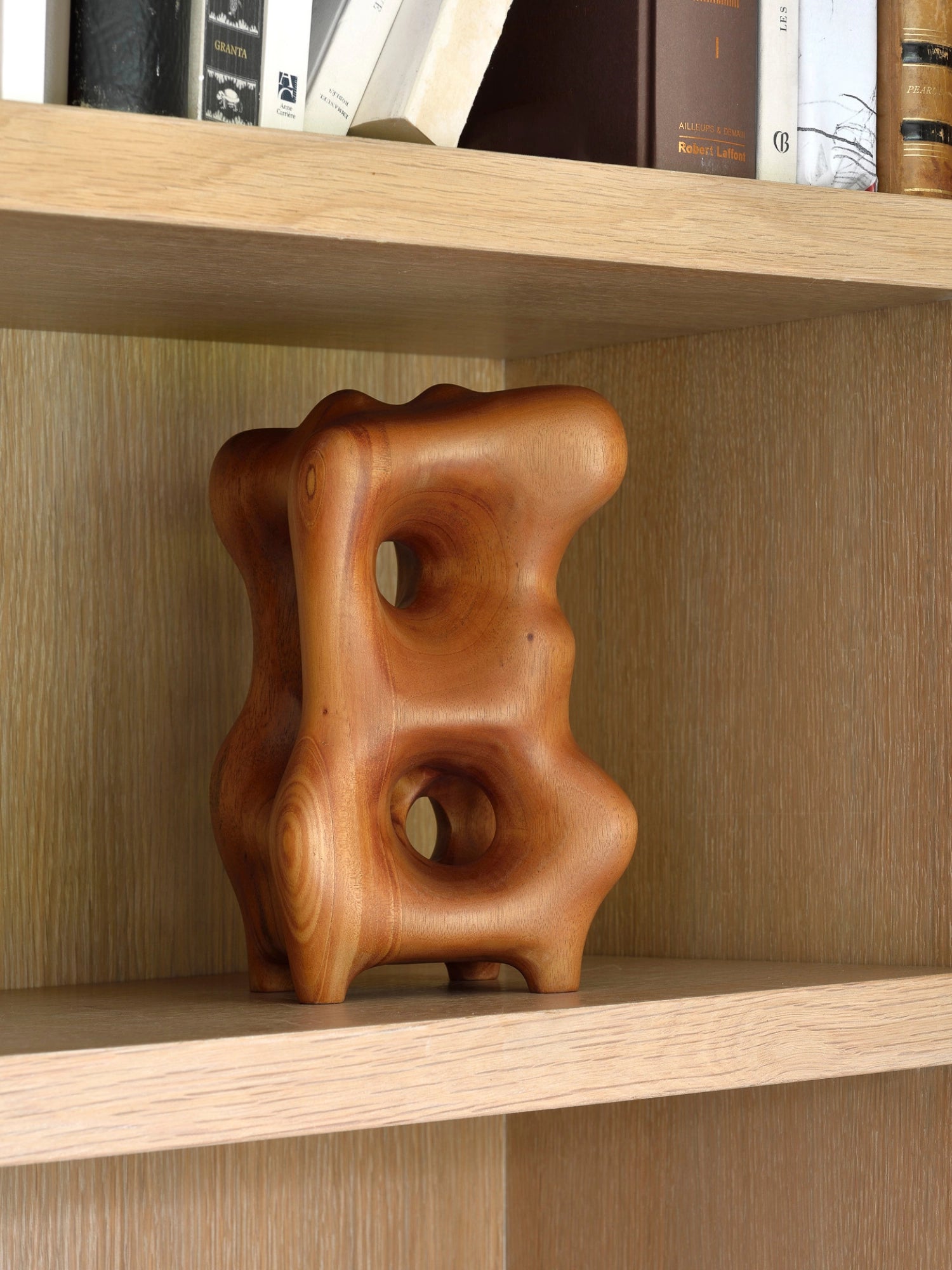 Ethnicraft Natural Organic Sculpture, an exquisite mahogany wood art piece with a warm, inviting brown color, featuring a unique, flowing design with carved details, nestled within a light wooden bookshelf.