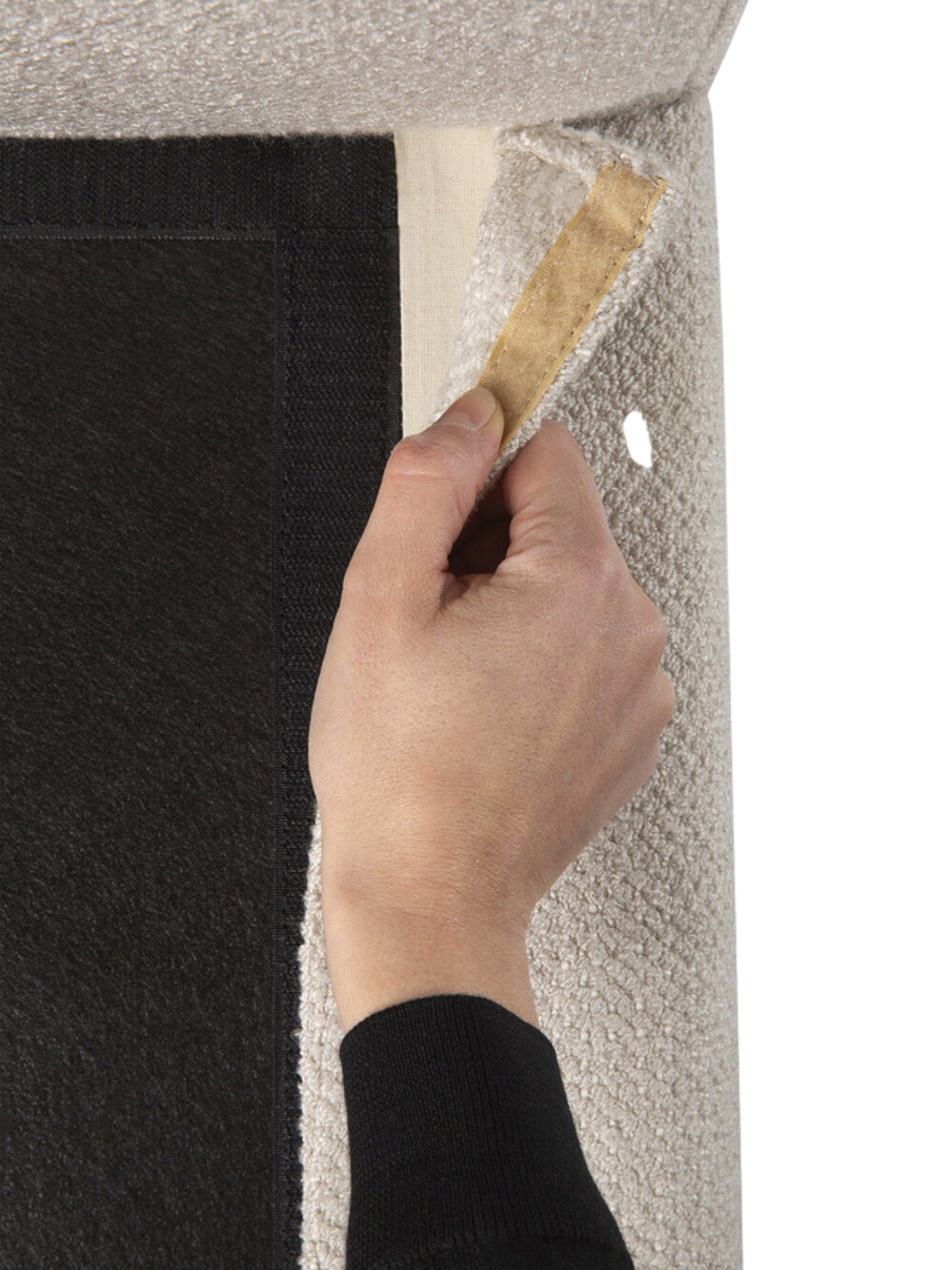 Ethnicraft Mellow Modular Sofa detail, a hand lifting the light beige textured fabric cover to reveal the secure Velcro fastening underneath. This demonstrates the sofa's practical and user-friendly design for easy maintenance.