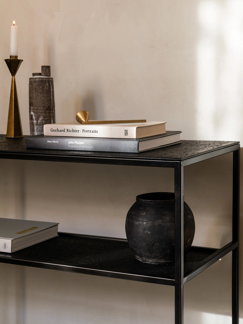 Ethnicraft Pentagon Console in Whisky finish, detailed shot showing books and decorative objects on its dark, textured surface and lower shelf. The elegant console features a modern black metal frame in a stylish interior.