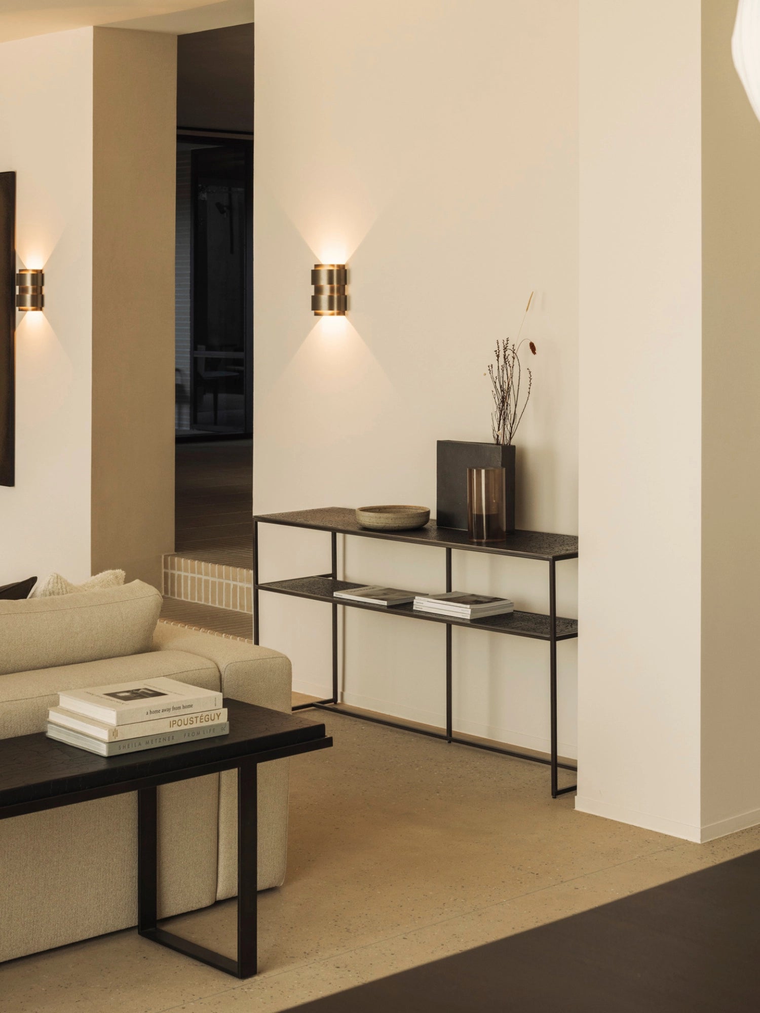 Ethnicraft Pentagon Console in Whisky finish, styled in a contemporary living room. The dark, textured console with its sleek metal frame holds decorative items, complementing the neutral-toned sofa and warm lighting.