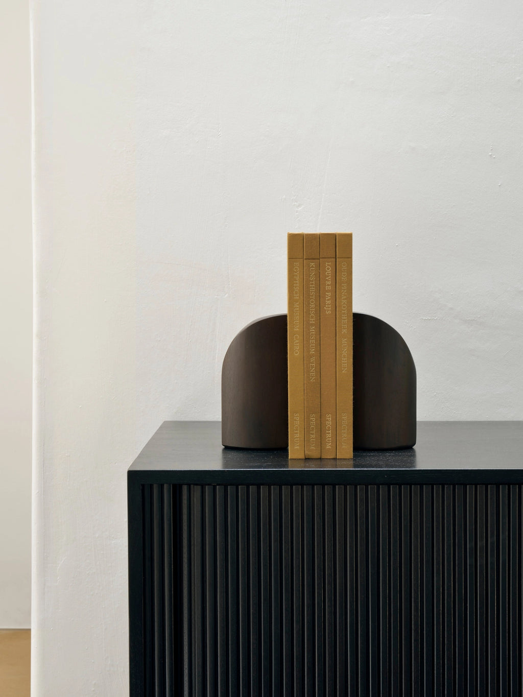 Ethnicraft PI Bookends in Mahogany Dark Brown, styled in a modern living space, holding a collection of books on a dark, textured cabinet, highlighting their functional and aesthetic appeal.