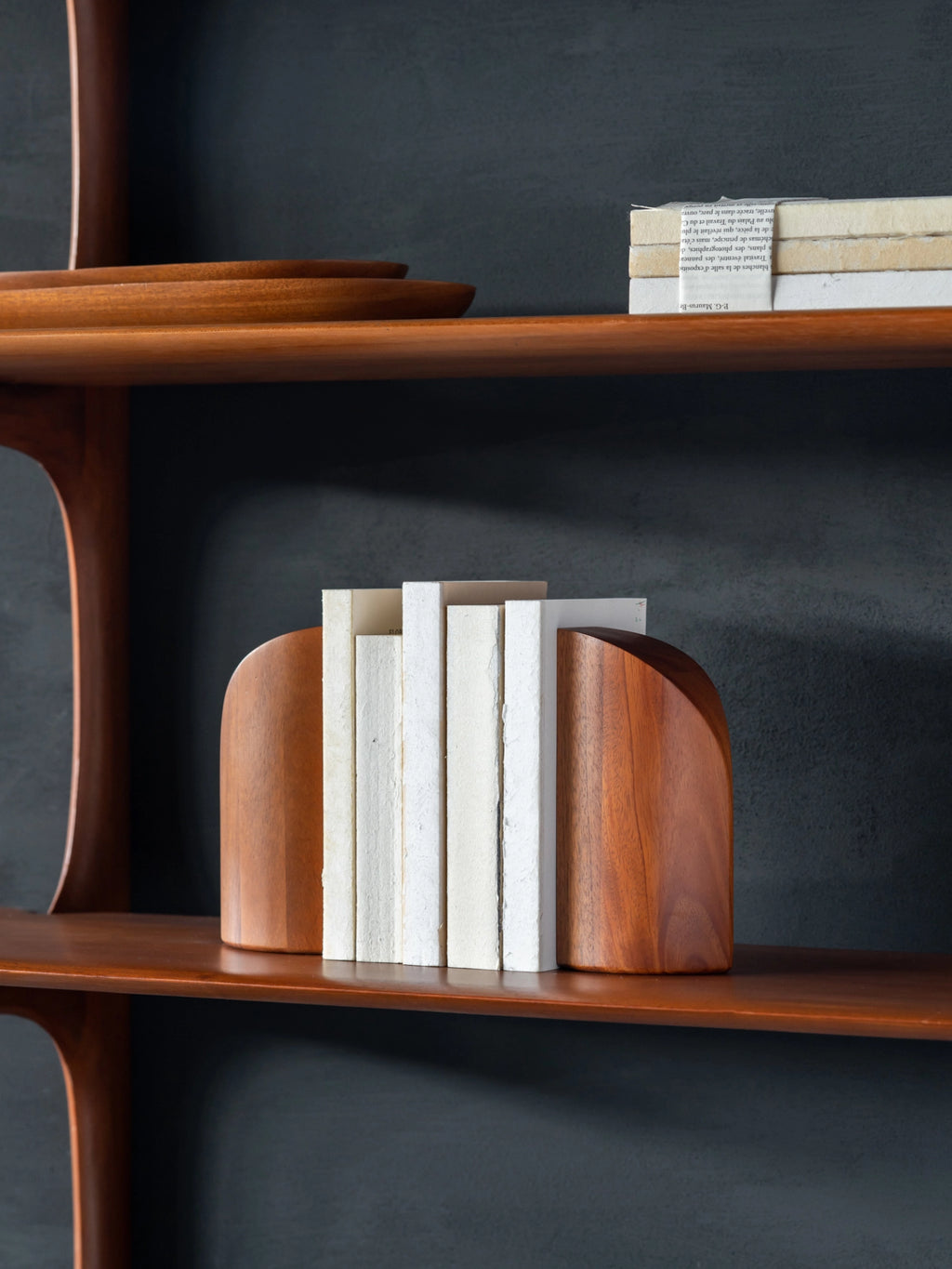 Ethnicraft PI Bookends, mahogany wood, displayed on a wooden shelf, holding a collection of white books, showcasing their functional and aesthetic appeal in a modern living space.