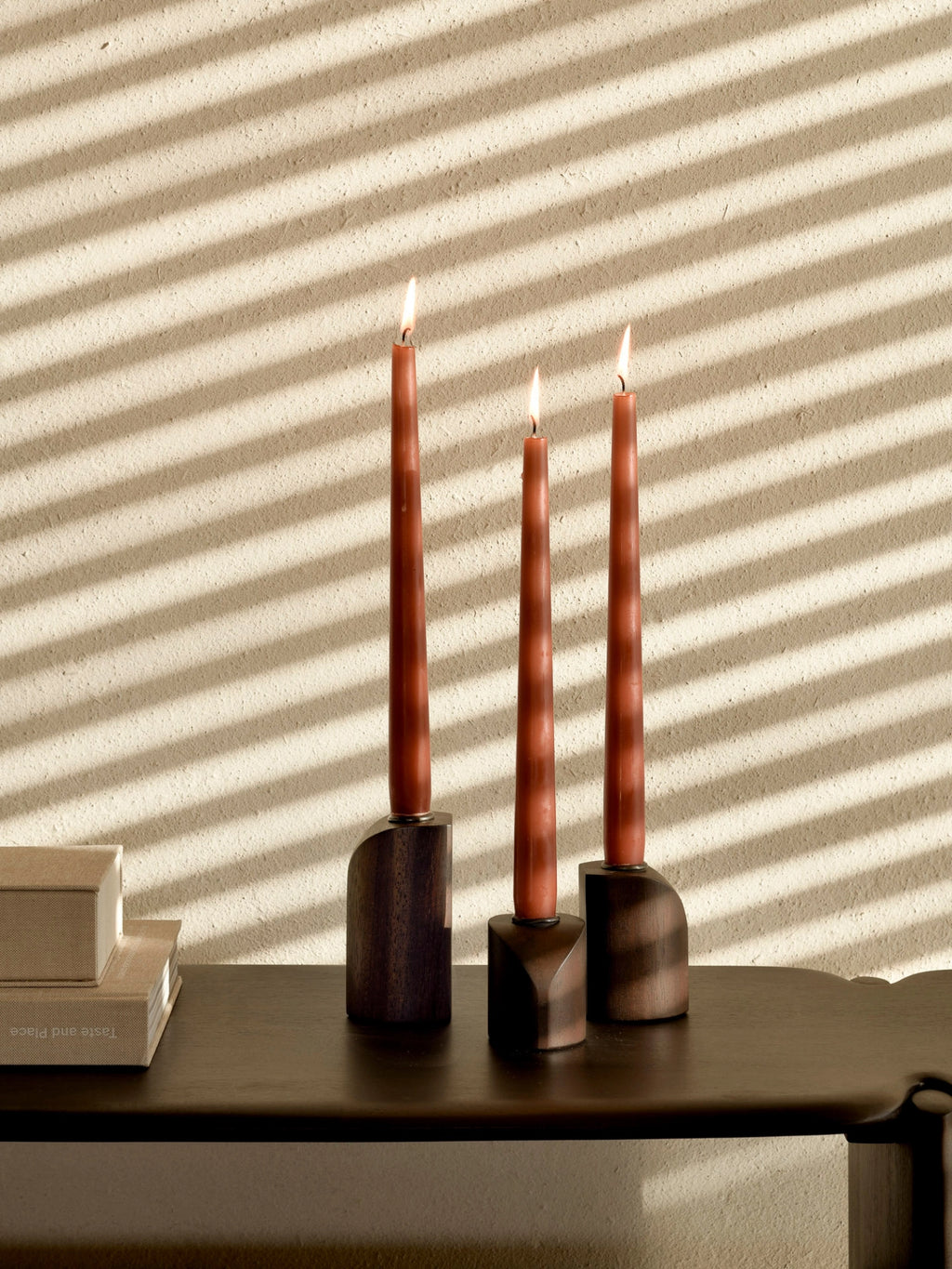 Ethnicraft PI Candle Holders - Set of 3, dark brown mahogany wood, with burning red taper candles, creating a warm, inviting ambiance in a stylish, sunlit room.