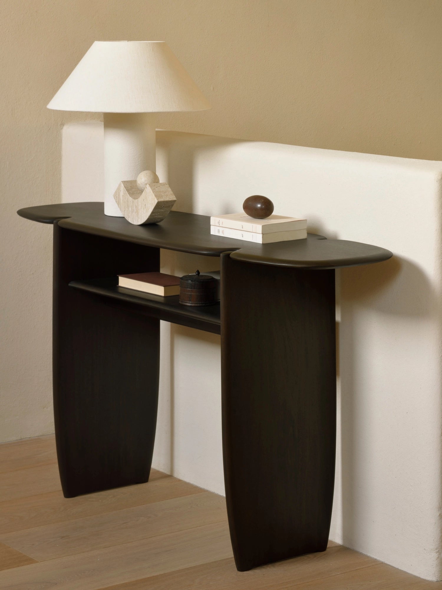 Ethnicraft PI Console in rich dark brown mahogany, highlighting its smooth, curved edges and practical lower shelf, beautifully styled with a lamp and decor in a cozy interior setting.
