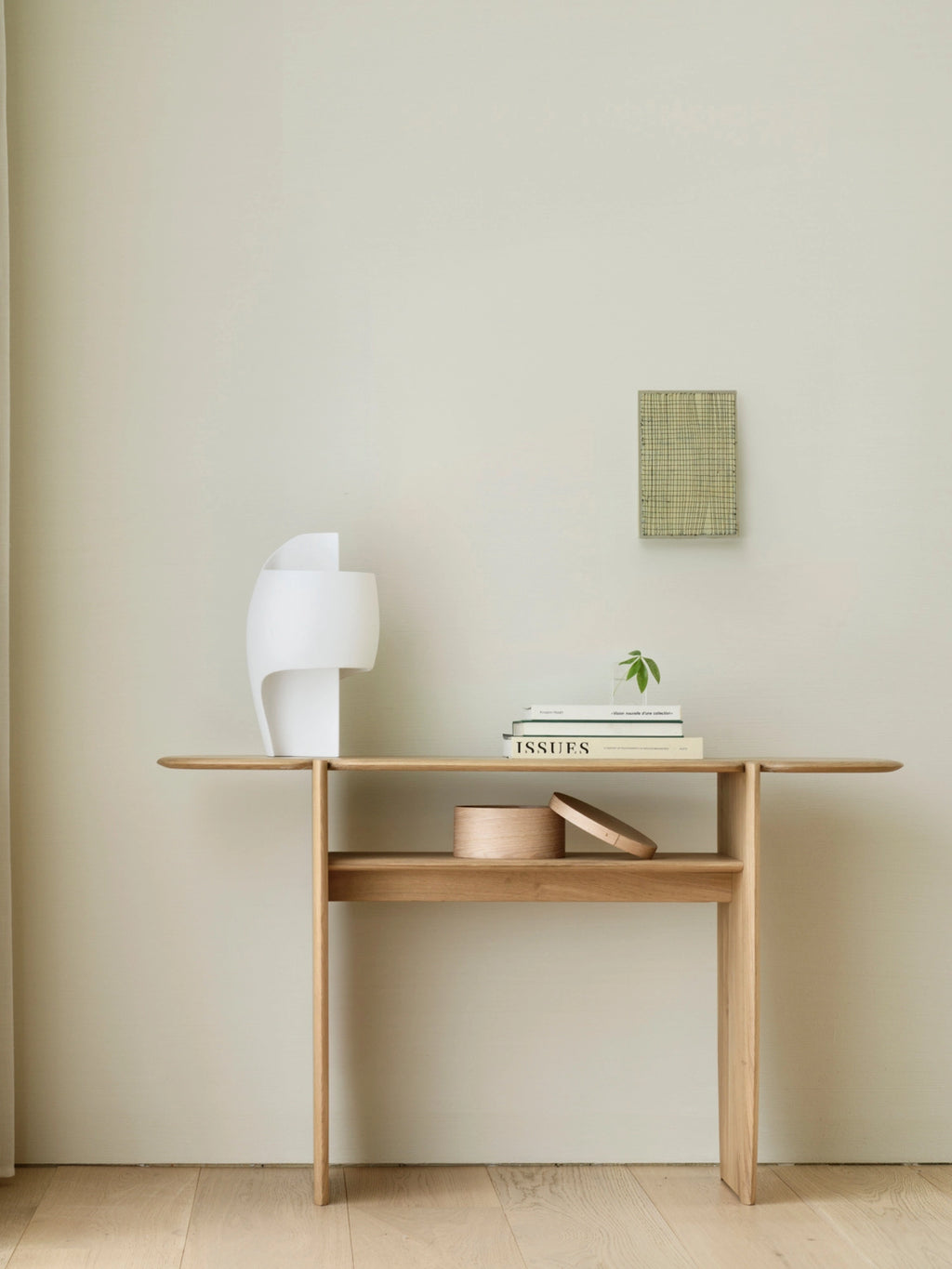Ethnicraft PI Console in natural oak, a beautiful and functional piece, styled in a contemporary living space, showcasing its light wood finish, lower shelf, and elegant design against a neutral wall.