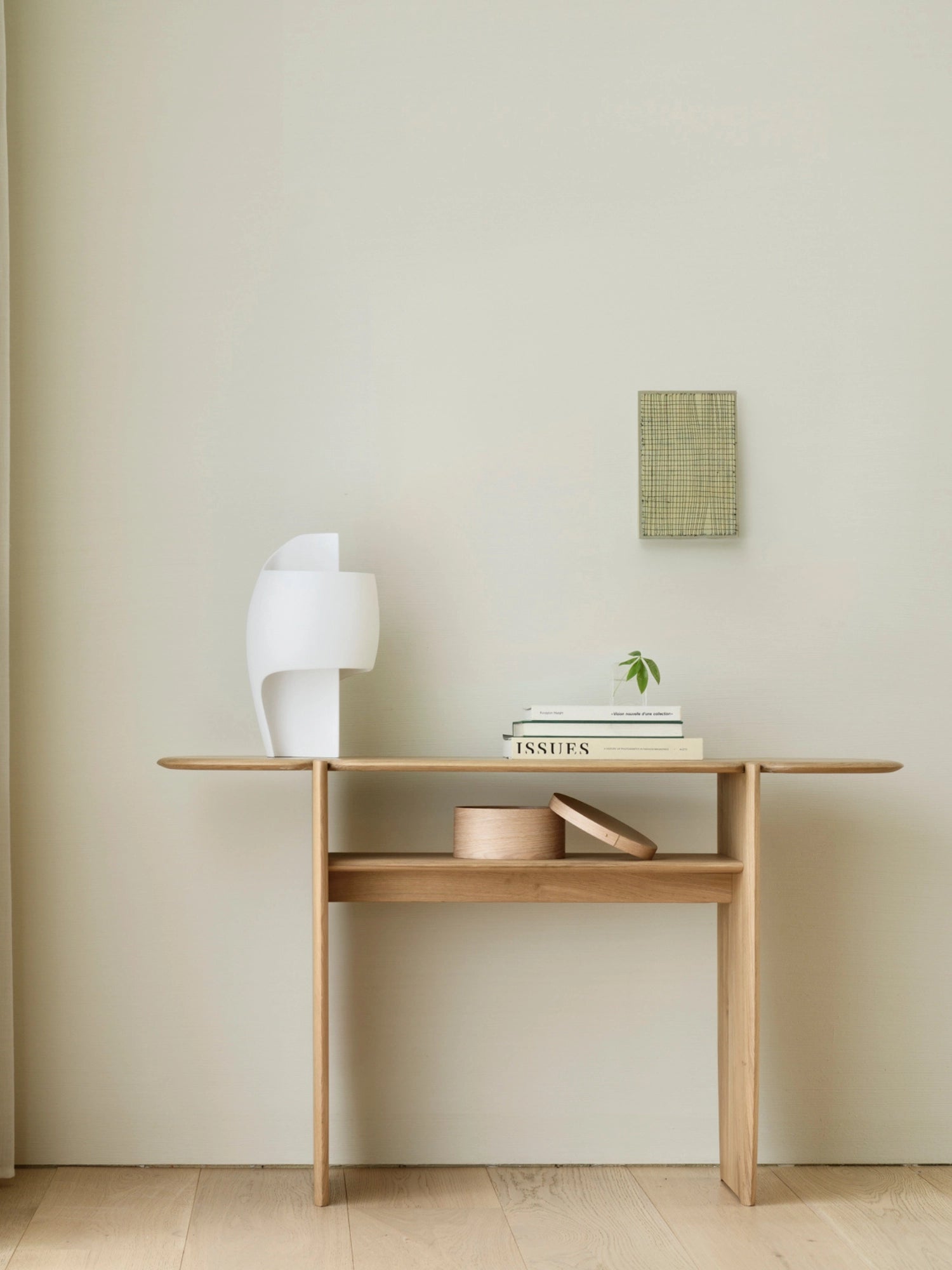 Ethnicraft PI Console in natural oak, a beautiful and functional piece, styled in a contemporary living space, showcasing its light wood finish, lower shelf, and elegant design against a neutral wall.