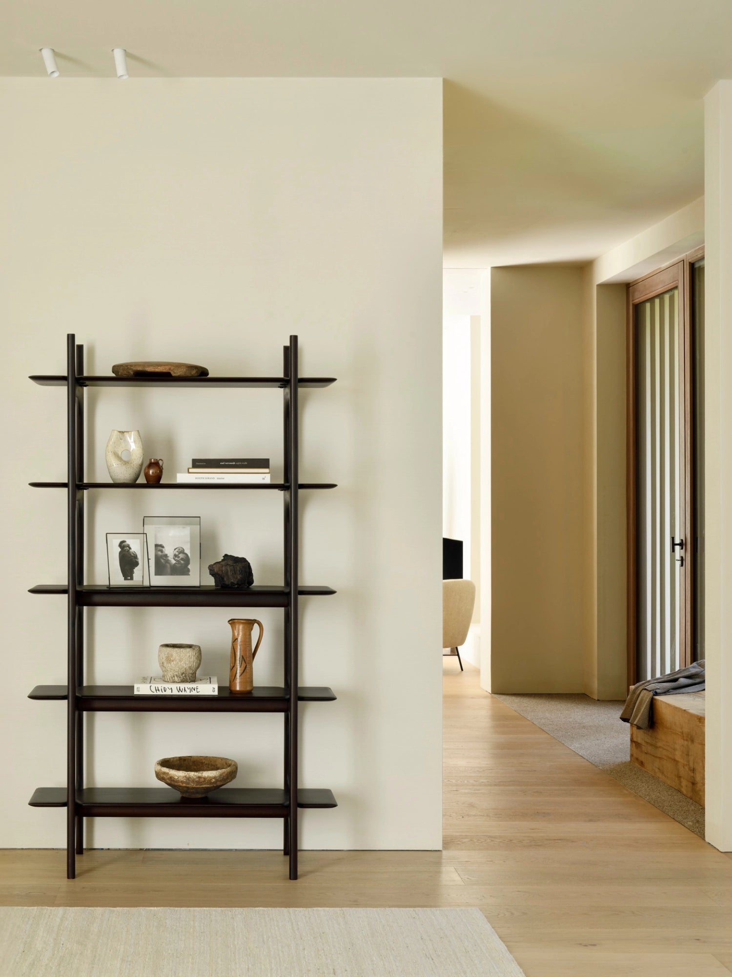 Ethnicraft PI Rack in dark brown mahogany, a sophisticated, tall shelving unit with five open shelves, displaying books and pottery, positioned in a spacious, sunlit room.