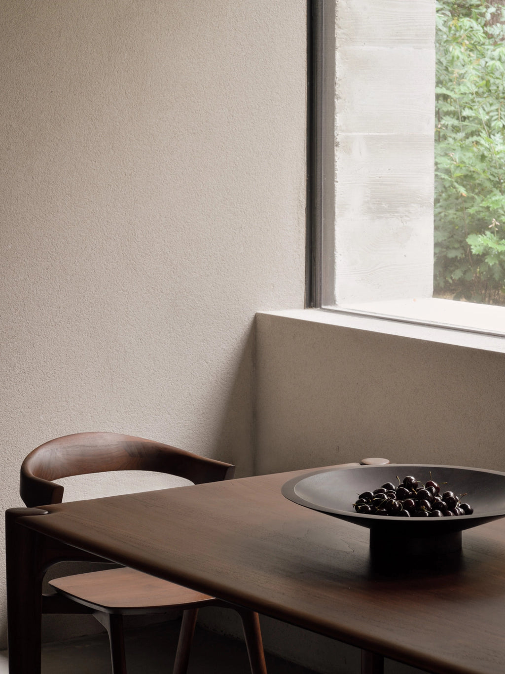 Ethnicraft Satellite Bowl in Mahogany Dark Brown, a wide, dark brown wooden bowl filled with dark berries, elegantly placed on a solid dark wood dining table in a modern setting, showcasing its versatile and sophisticated appeal.