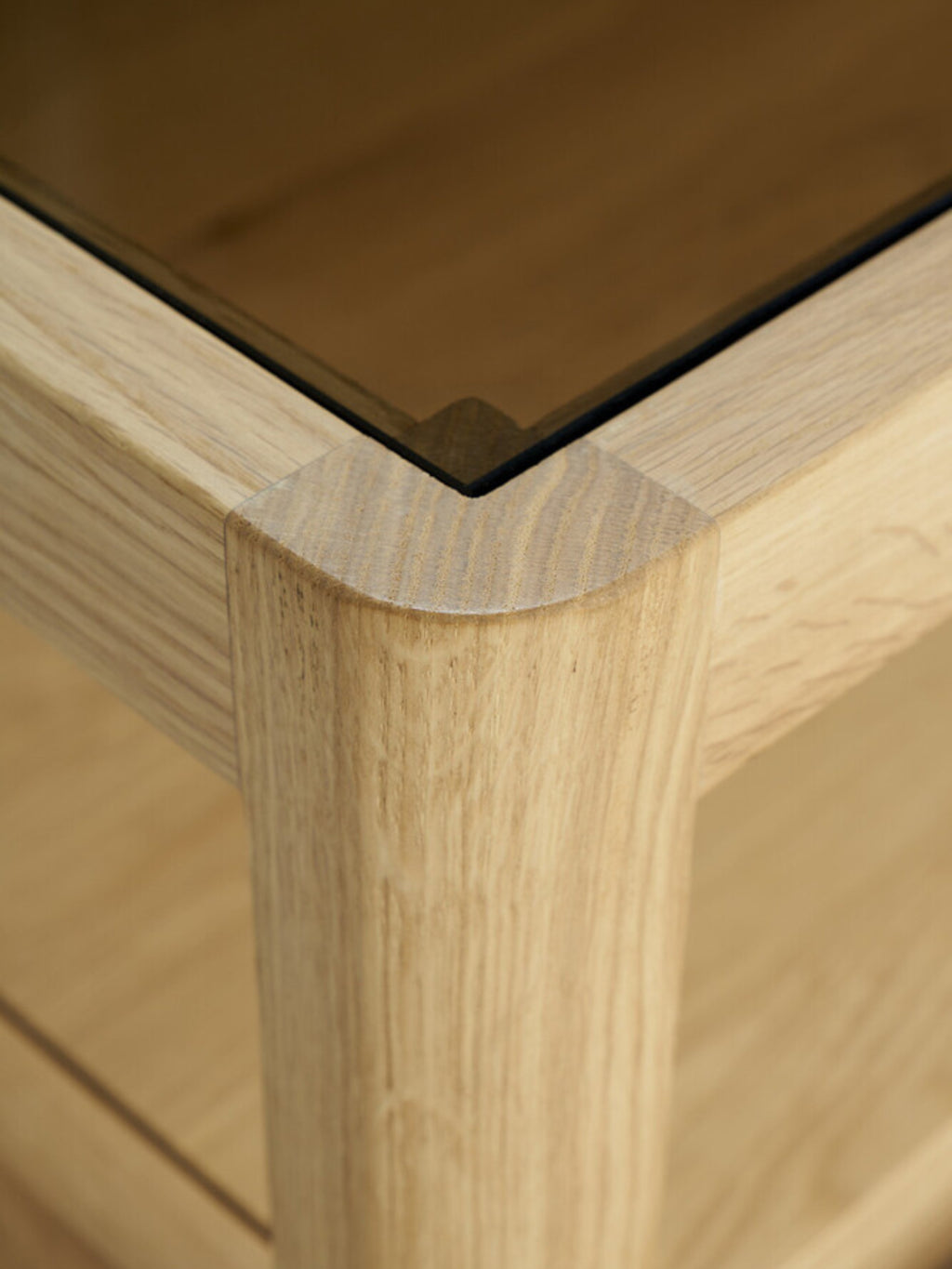 Ethnicraft Spindle Dresser in natural oak, a close-up detail of the rounded corner and leg, showcasing the smooth wood texture and premium craftsmanship with a glass top.