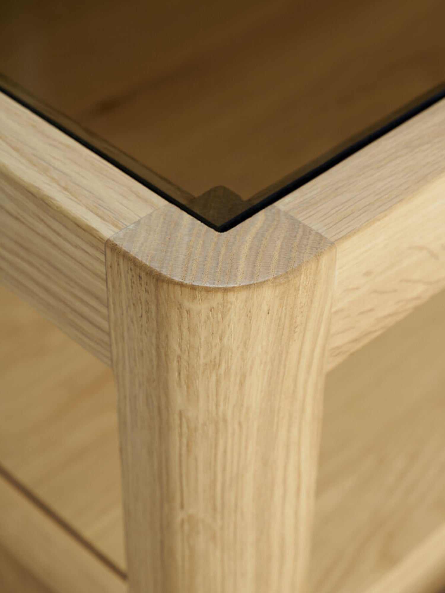 Ethnicraft Spindle Dresser in natural oak, a close-up detail of the rounded corner and leg, showcasing the smooth wood texture and premium craftsmanship with a glass top.
