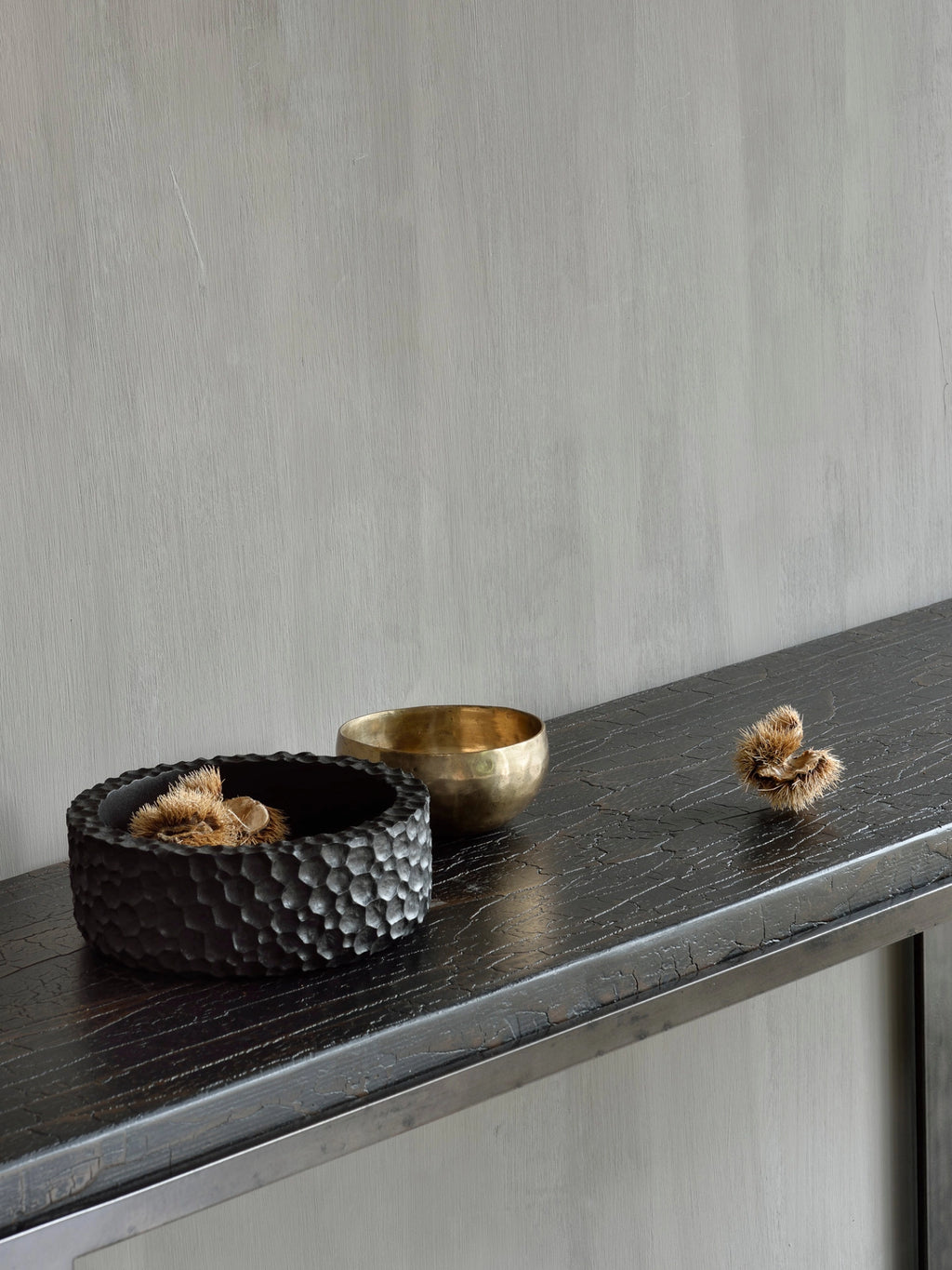 Close-up of the Ethnicraft Stability Console's dark brown textured surface, displaying decorative items like a carved black bowl and a golden bowl. The console's elegant finish and sturdy design are highlighted in this stylish setting.