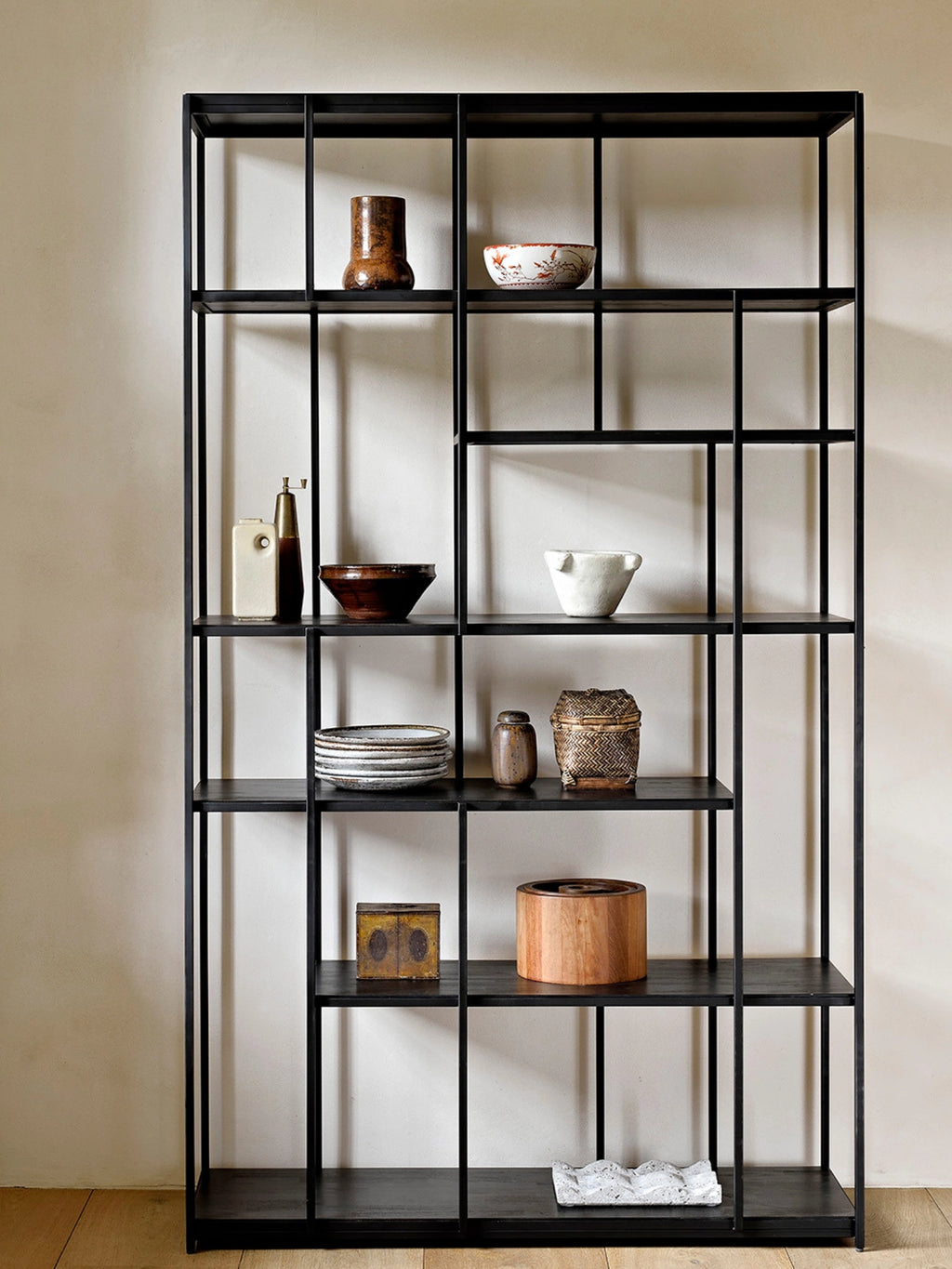 Ethnicraft Studio Rack, a stylish black metal shelving unit with an open, geometric design, filled with various decorative objects and books, enhancing a contemporary living space.