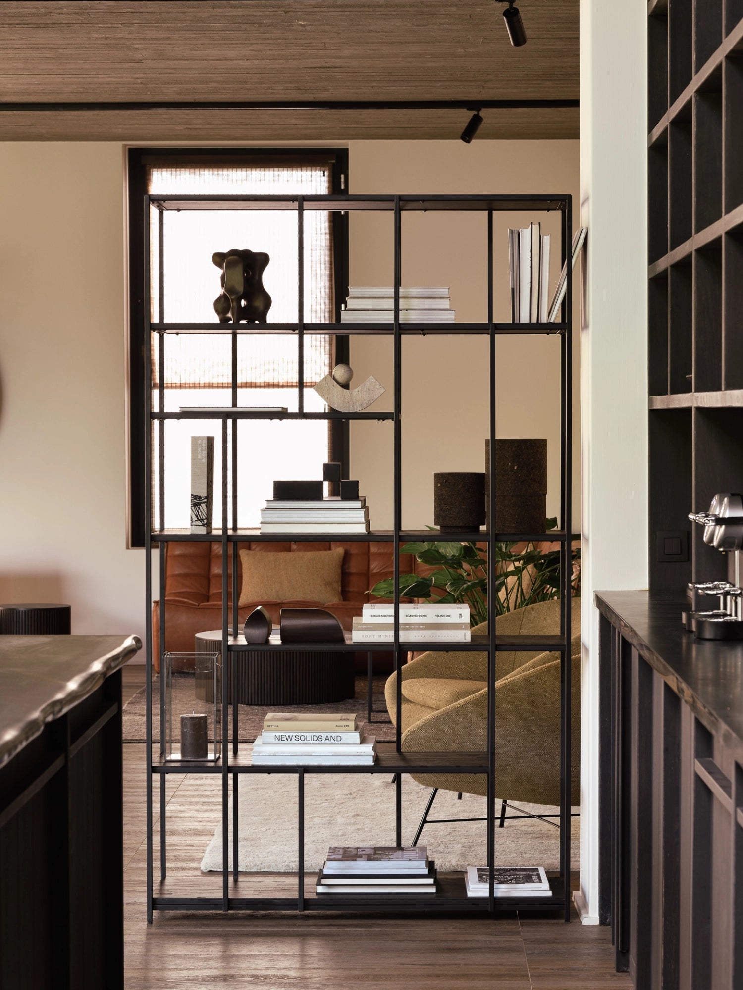 Ethnicraft Studio Rack in black teak, a stylish and versatile room divider with multiple shelves, adorned with books and decorative objects, in a contemporary living space.