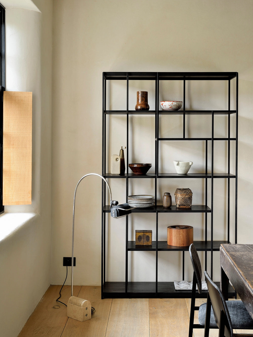 Ethnicraft Studio Rack in black teak, a tall, modern shelving unit with an asymmetrical grid design, filled with various decorative items, positioned in a spacious, well-lit room.