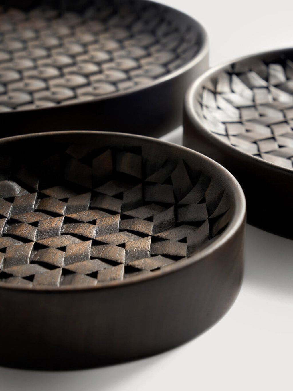 Ethnicraft Tampa Boards Set, a close-up detail of the smallest dark brown wooden serving board, highlighting its intricate geometric woven pattern and smooth, rounded edges on a white surface.