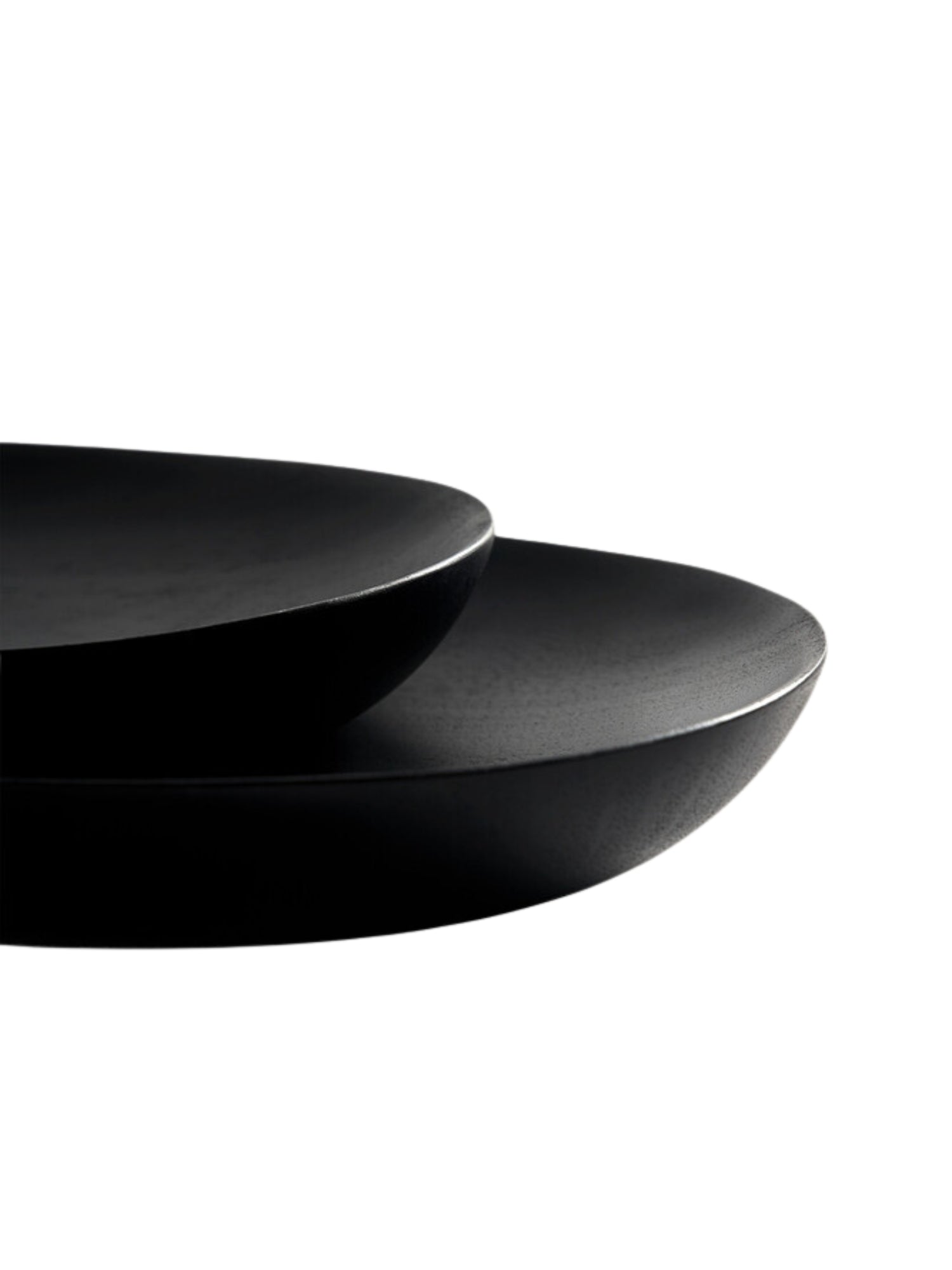 Ethnicraft Thin Oval Boards Set in mahogany black, a close-up detail shot revealing the subtle curve and thin edge of two dark, smooth oval boards, stacked slightly, against a crisp white background, showcasing their refined craftsmanship.