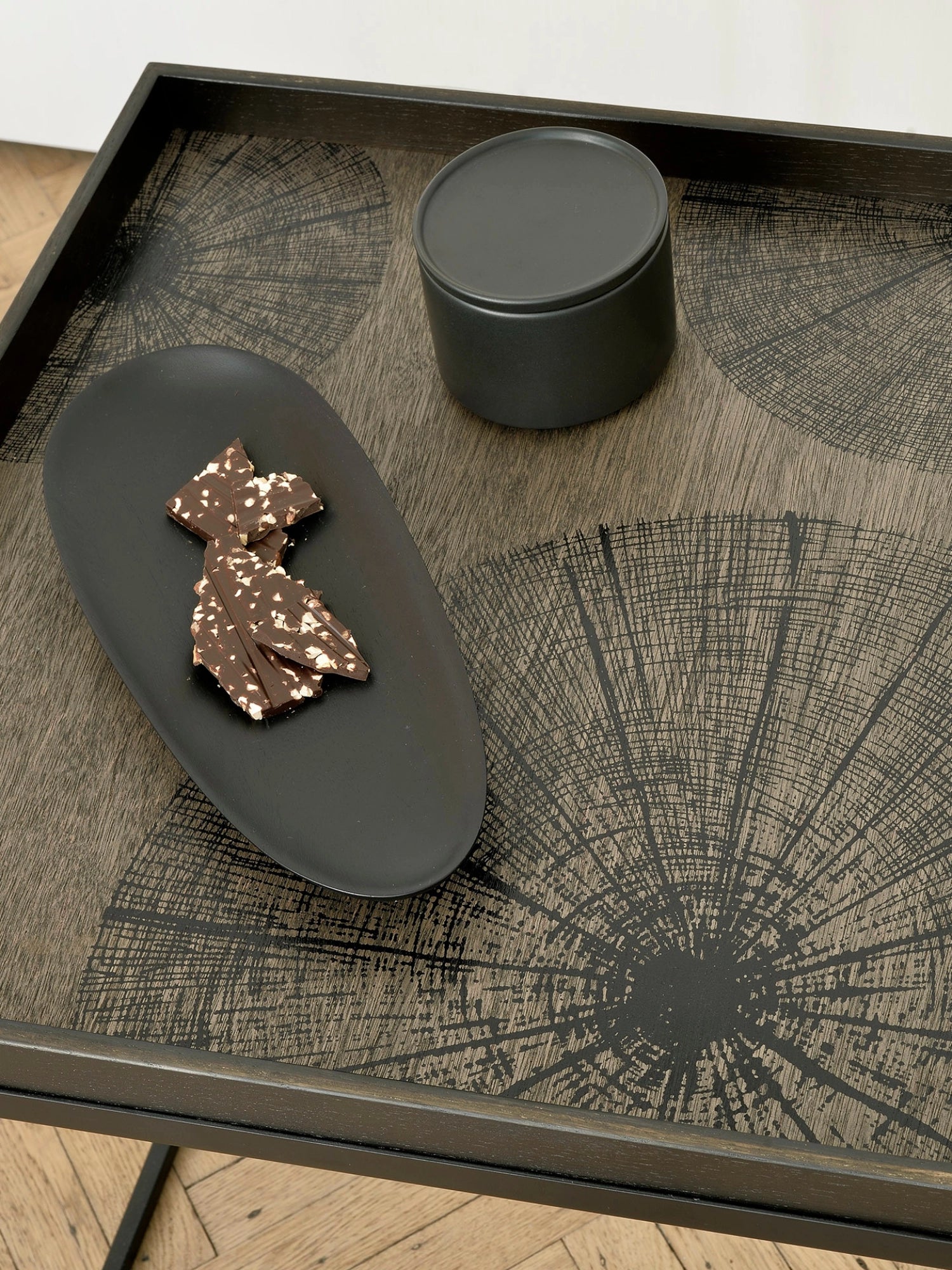 Ethnicraft Thin Oval Boards Set in mahogany black, featuring a large oval board with intricate circular patterns, holding chocolate pieces and a small black container, displayed on a dark wooden table with a light background.