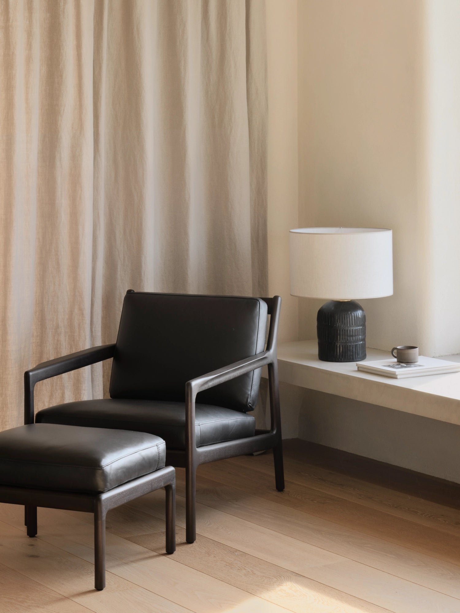 Ethnicraft Jack Lounge Chair, a modern minimalist armchair featuring a dark solid wood frame with clean lines and open armrests, upholstered in plush black leather cushions for ultimate comfort. This contemporary living room chair is paired with a matching black leather ottoman, creating a sophisticated reading nook or stylish accent for modern Scandinavian interiors.