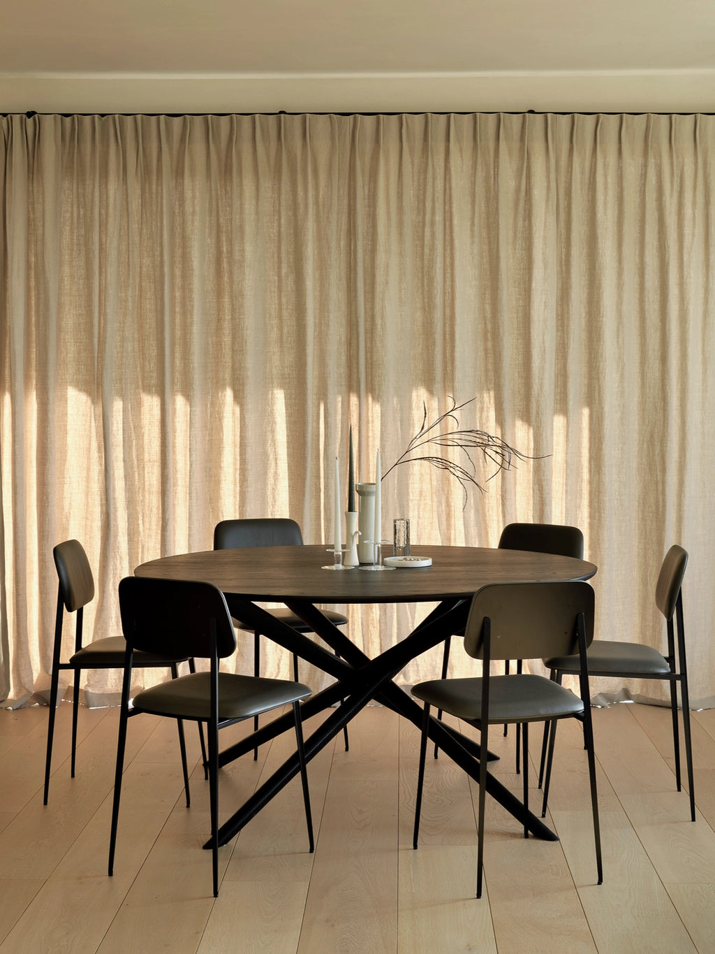 Ethnicraft Mikado Dining Table, a contemporary oval dining table crafted from rich dark solid wood, likely stained oak, featuring a smooth finish and elegant rounded edges. Its striking matte black metal X-shaped base provides a modern minimalist aesthetic and sturdy support for comfortable dining. This stylish dark wood dining table is perfect for modern dining rooms, industrial chic interiors, or as a sophisticated centerpiece for family gatherings.