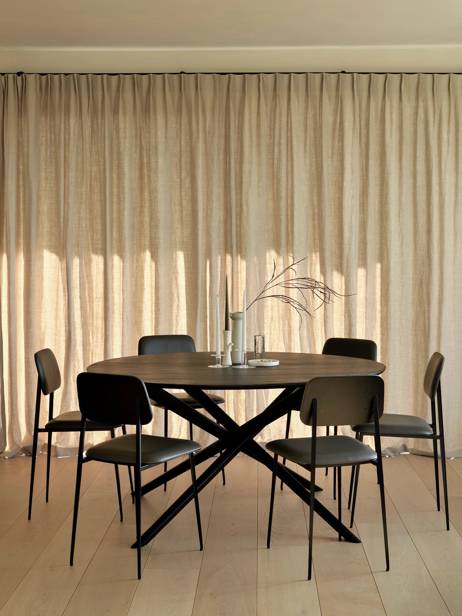 Ethnicraft Mikado Dining Table, a contemporary oval dining table crafted from rich dark solid wood, likely stained oak, featuring a smooth finish and elegant rounded edges. Its striking matte black metal X-shaped base provides a modern minimalist aesthetic and sturdy support for comfortable dining. This stylish dark wood dining table is perfect for modern dining rooms, industrial chic interiors, or as a sophisticated centerpiece for family gatherings.