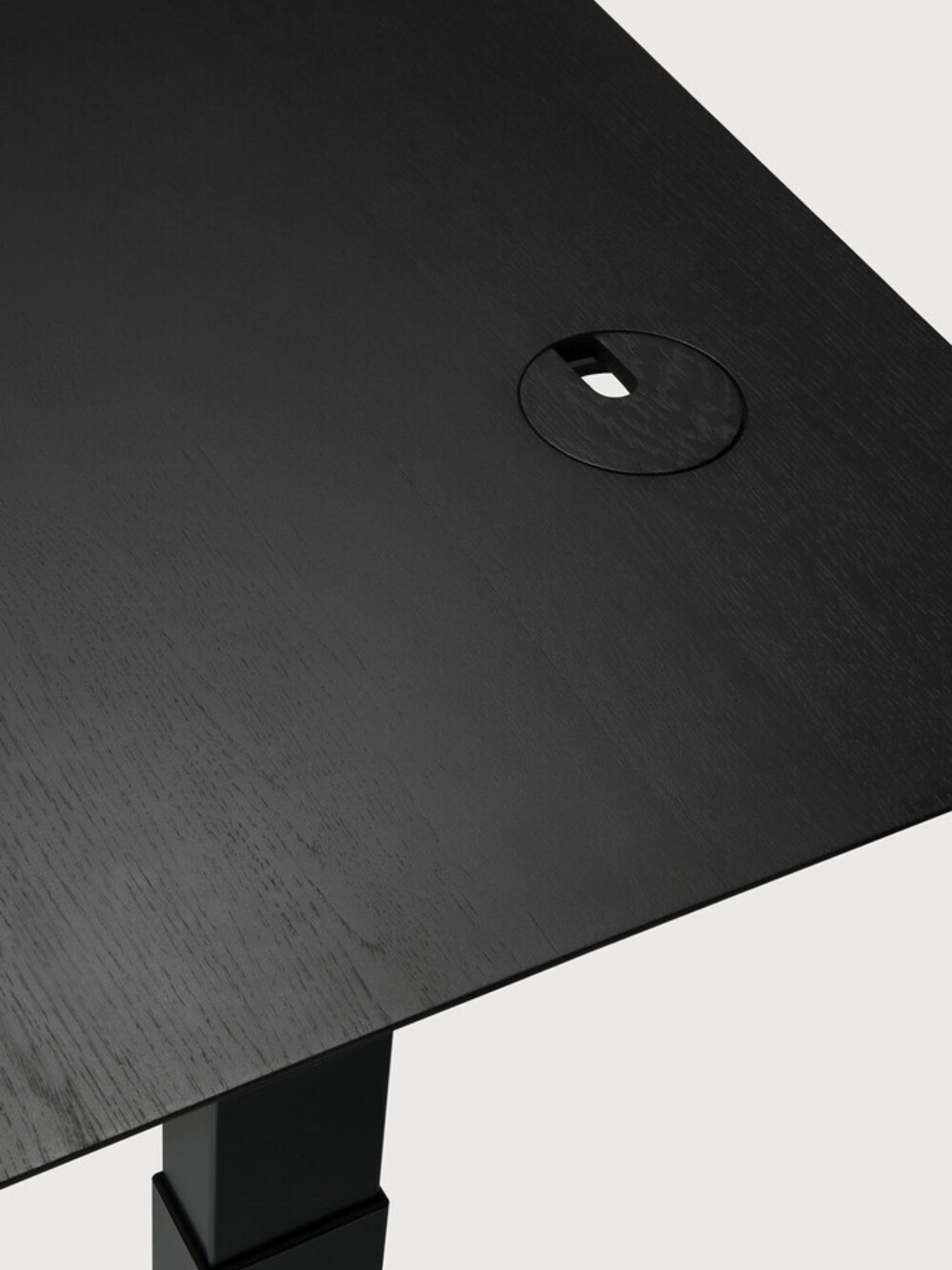 Ethnicraft Bok Adjustable Desk with black oak tabletop and black frame, a close-up of the smooth, dark wood surface with a subtle grain texture and a neat, circular cable management grommet.