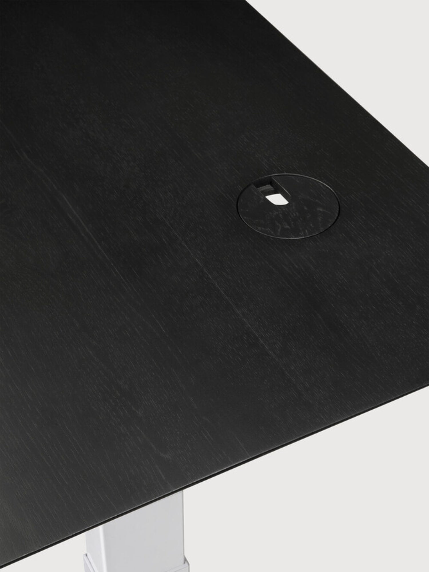 Ethnicraft Bok Adjustable Desk, a detailed close-up of the black oak tabletop, highlighting the rich wood grain texture and a circular cable management grommet. This premium, minimalist design offers both style and practicality.