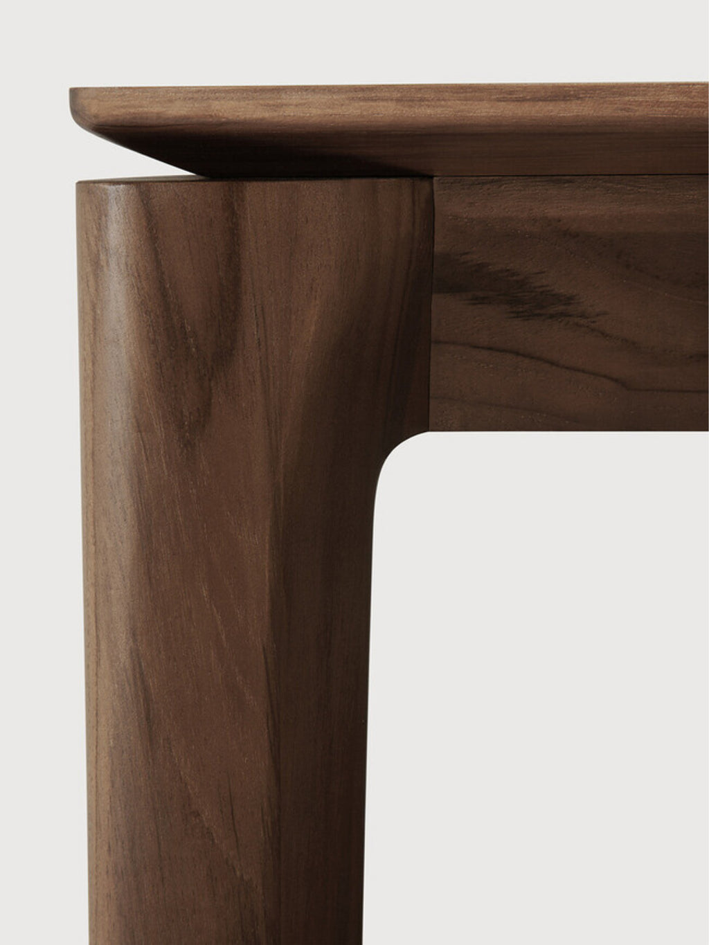 Ethnicraft Bok Dining Table in Teak Brown, showcasing a close-up detail of the rich, warm brown wood grain and smooth, curved edges of the table leg and tabletop, highlighting the premium craftsmanship and natural texture, displayed on a clean white background.