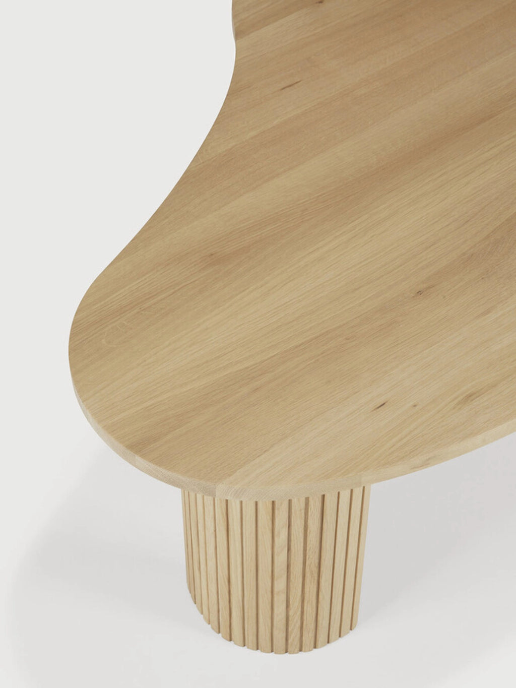 Ethnicraft Boomerang Coffee Table, a modern oak wood table with a unique curved, organic shape. Features a fluted, textured cylindrical leg, highlighting the natural grain and craftsmanship, displayed on a white background.