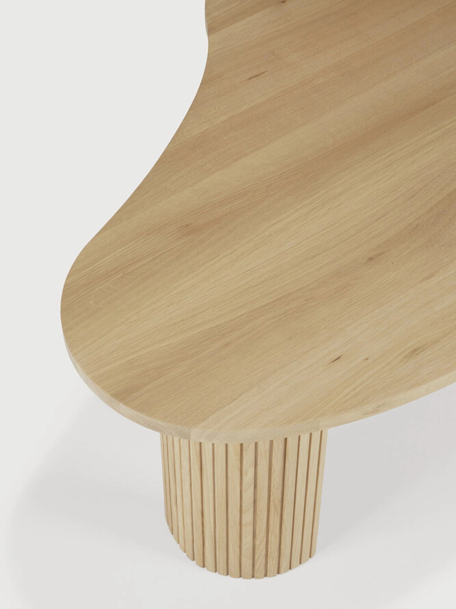Ethnicraft Boomerang Coffee Table, a modern oak wood table with a unique curved, organic shape. Features a fluted, textured cylindrical leg, highlighting the natural grain and craftsmanship, displayed on a white background.