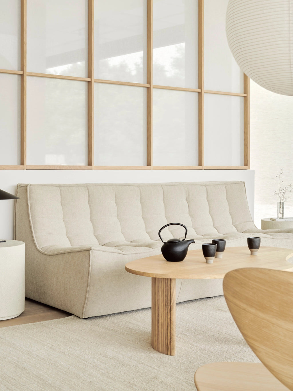 Ethnicraft Boomerang Coffee Table in natural oak, featuring a single table in a contemporary living room with a light-colored sofa, tea set, and natural light.