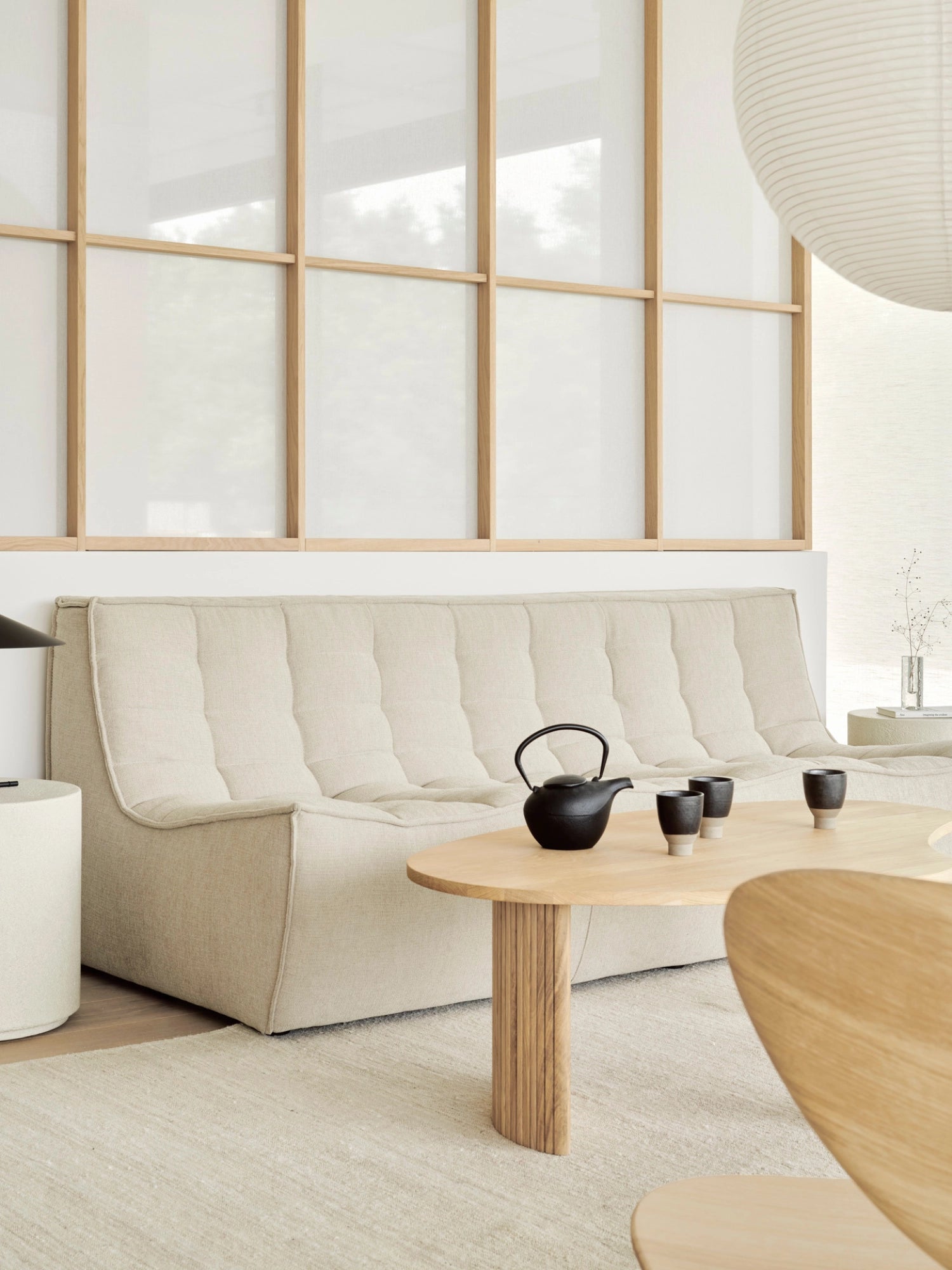 Ethnicraft Boomerang Coffee Table in natural oak, featuring a single table in a contemporary living room with a light-colored sofa, tea set, and natural light.