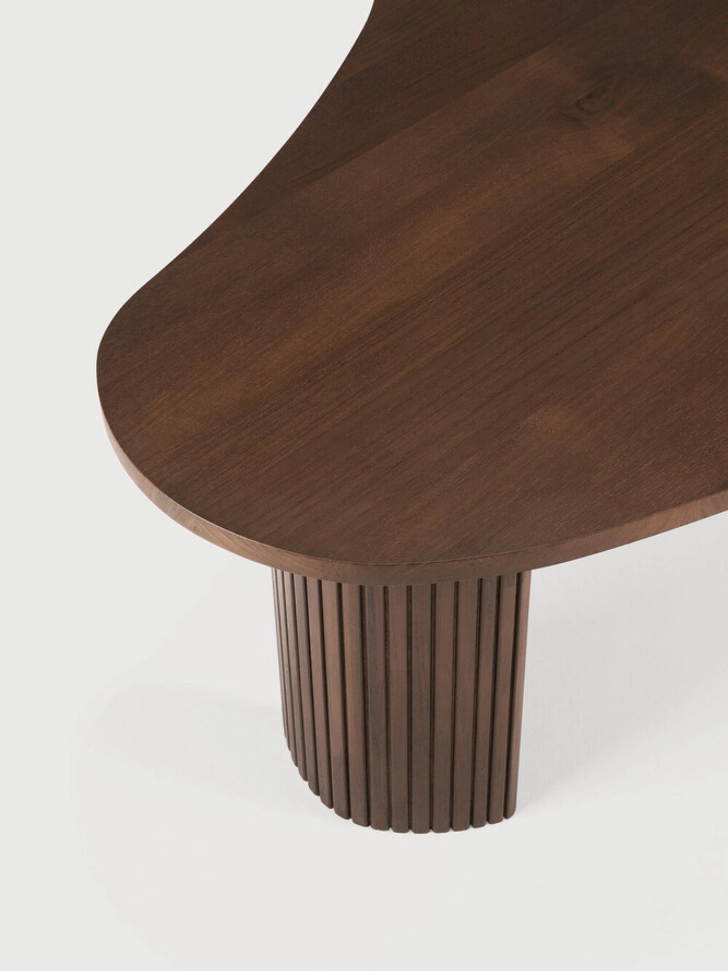 Ethnicraft Boomerang Coffee Table in dark brown teak, a close-up detail shot of the smooth, rounded edge of the tabletop meeting the finely ribbed, curved support leg, on a white background.