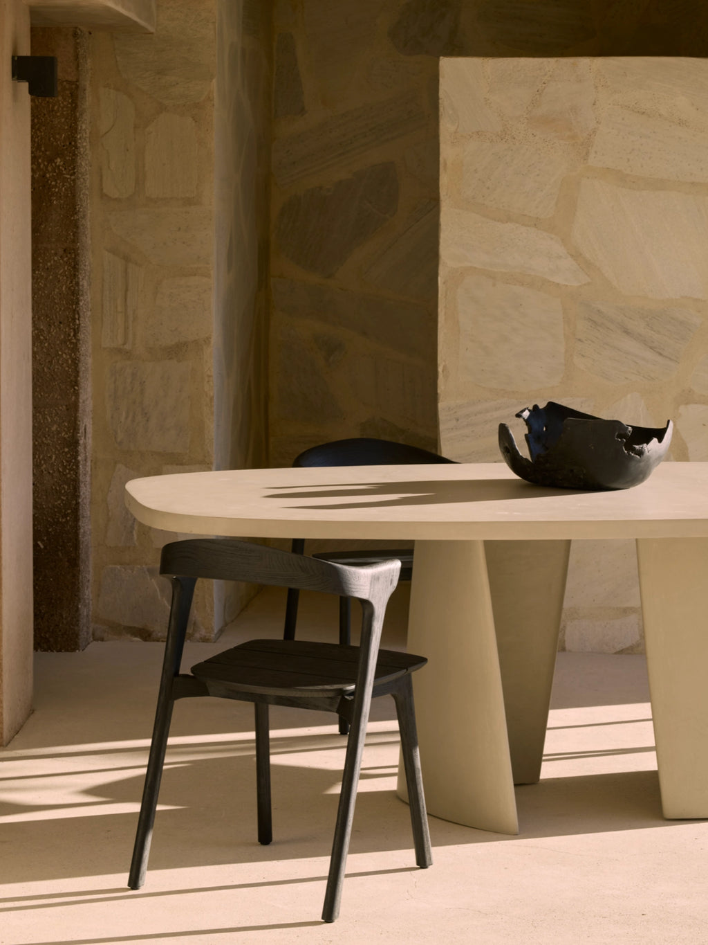 Ethnicraft Canyon Outdoor Dining Table, a minimalist organic modern dining table featuring a smooth, light beige microcement rounded rectangular top and two sculptural, tapered pedestal bases.