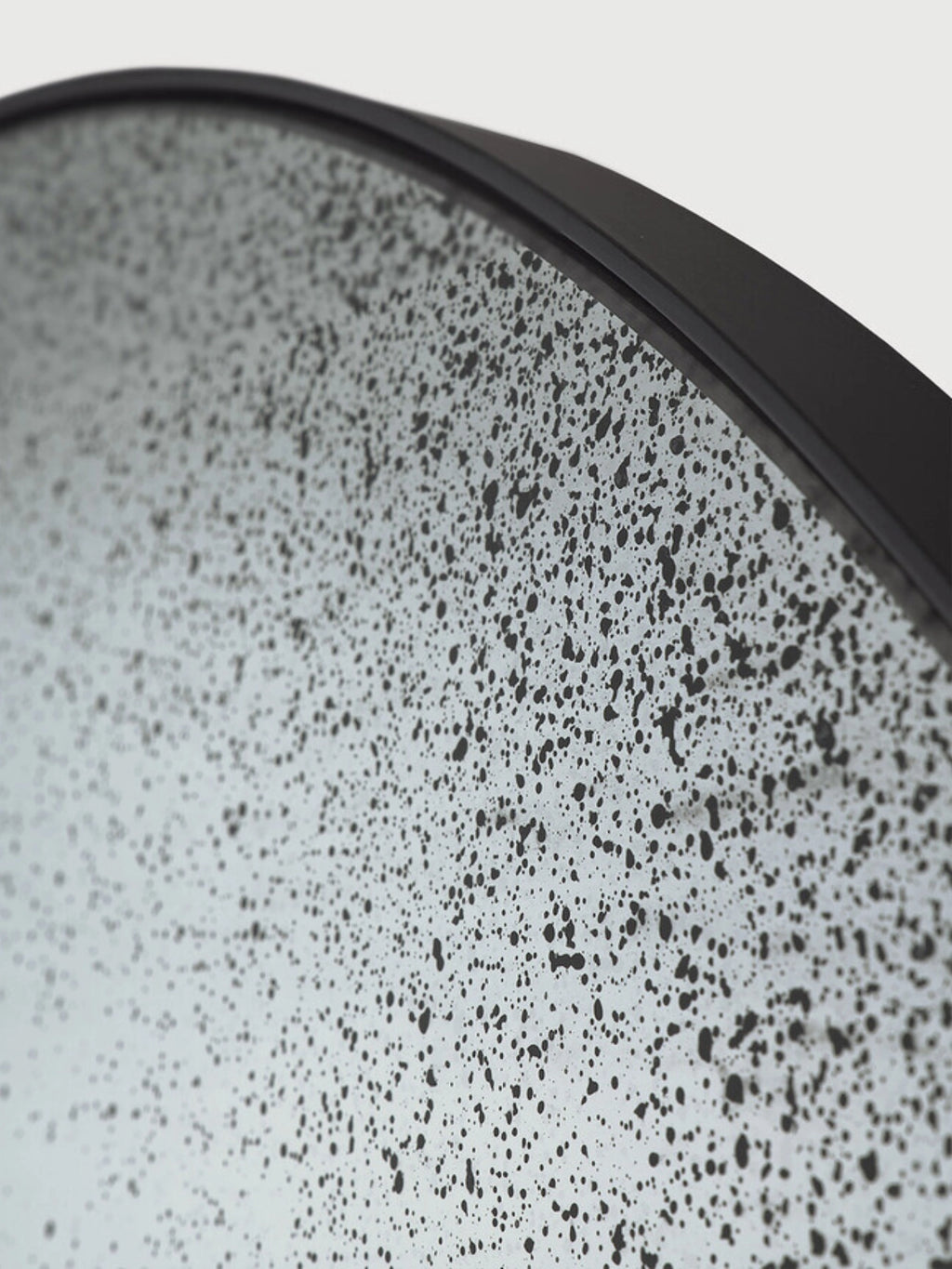 Ethnicraft Clear Gate Wall Mirror, a round industrial chic wall mirror featuring a unique distressed and speckled antique-finish glass surface set within a sleek matte black metal frame. This contemporary brutalist mirror makes a striking statement piece for living rooms, entryways, or modern industrial interiors.