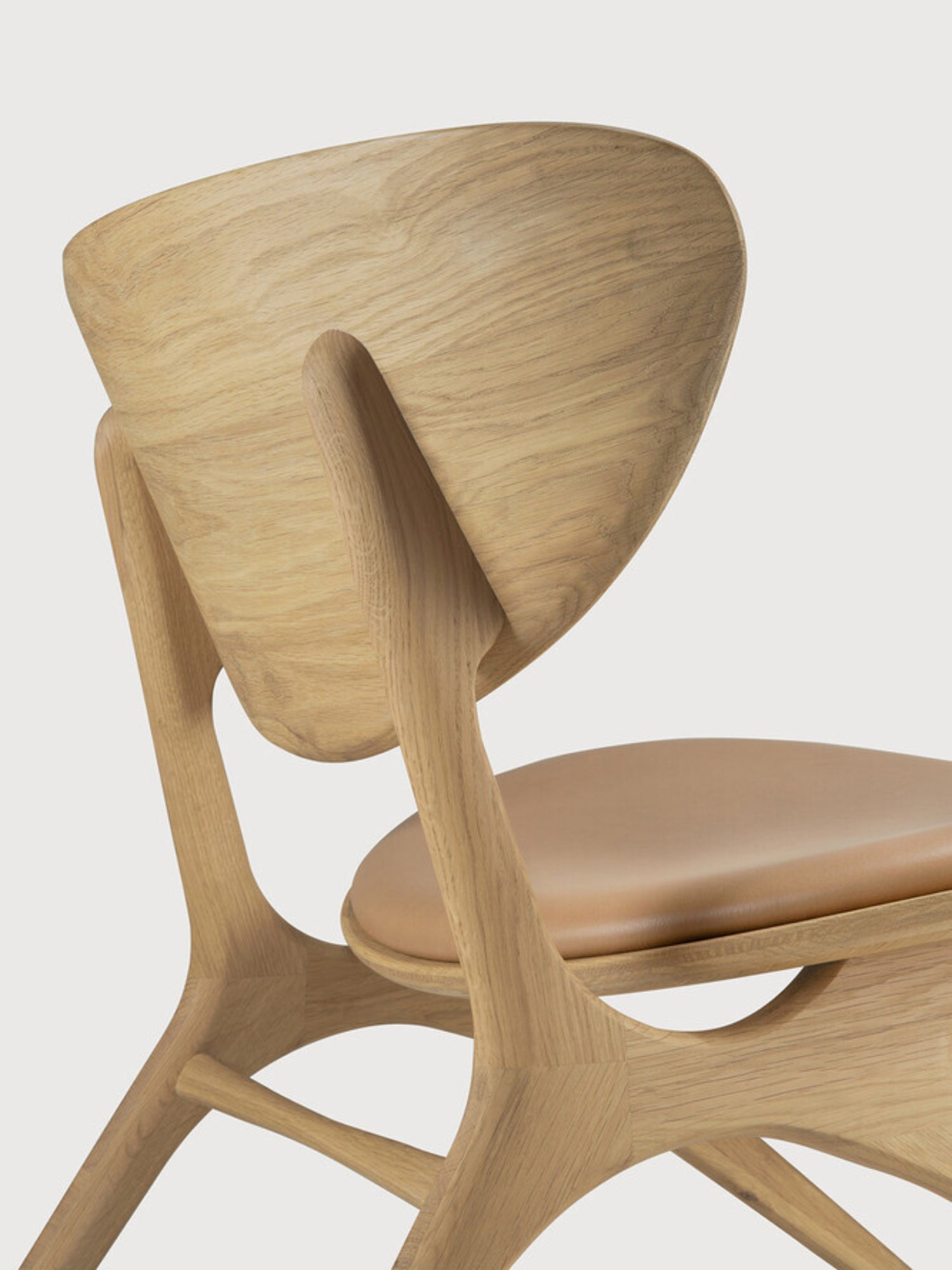 Ethnicraft Eye Lounge Chair, a striking organic modern lounge chair crafted from light natural solid oak with a fluid, sculptural frame and a gracefully curved backrest that embraces the body. It features a plush tan leather seat cushion, showcasing the beautiful natural wood grain and sleek, contemporary design. This minimalist solid oak and leather accent chair is perfect for a stylish living room, cozy reading nook, or sophisticated bedroom.