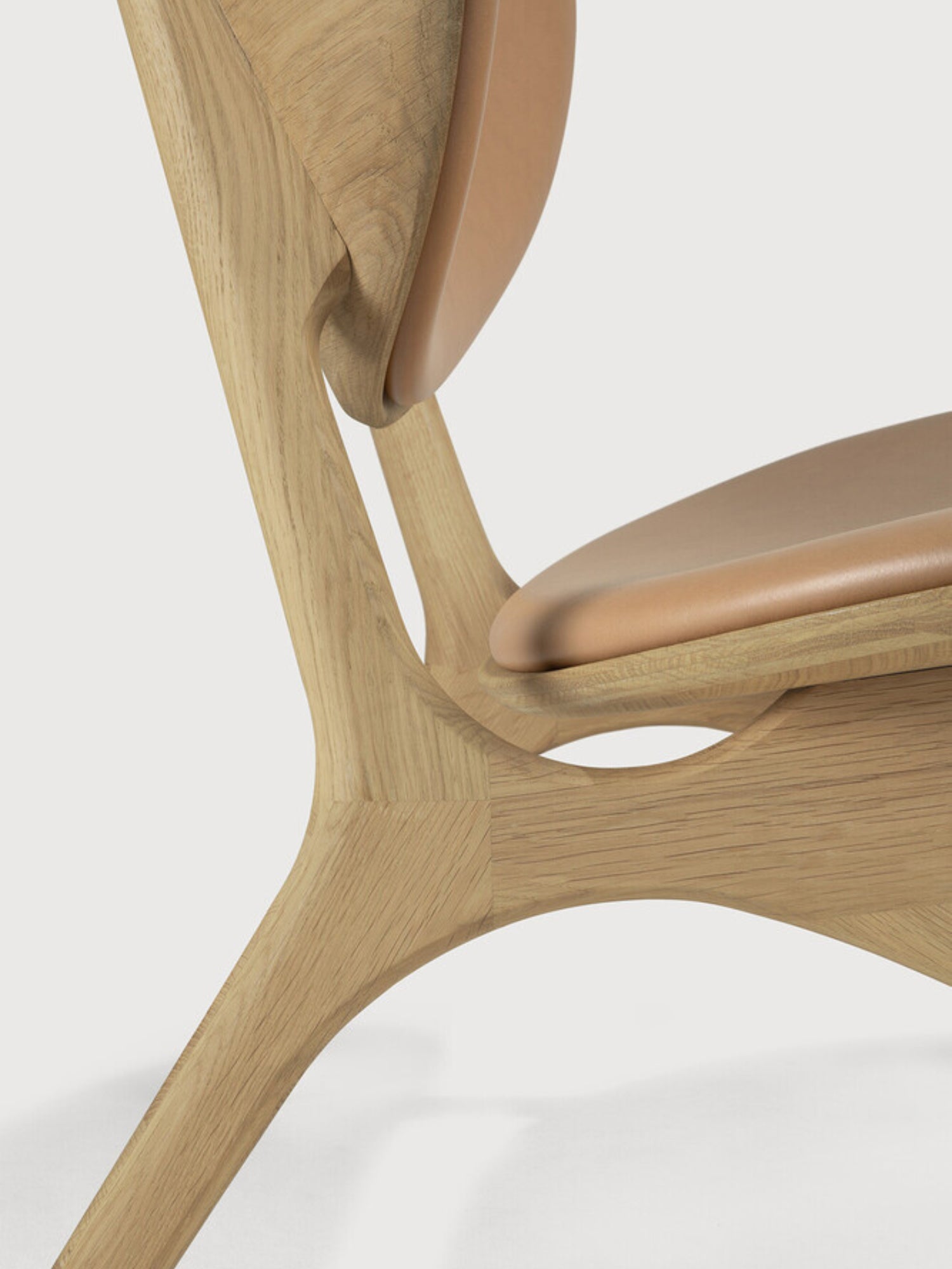 Ethnicraft Eye Lounge Chair, an organic modern solid oak lounge chair featuring a sculptural natural light wood frame with fluid, curved lines and a cantilevered design. It boasts a comfortable tan leather seat and backrest, showcasing minimalist elegance and exceptional craftsmanship. Perfect as a contemporary accent chair for a modern living room or a stylish reading nook.