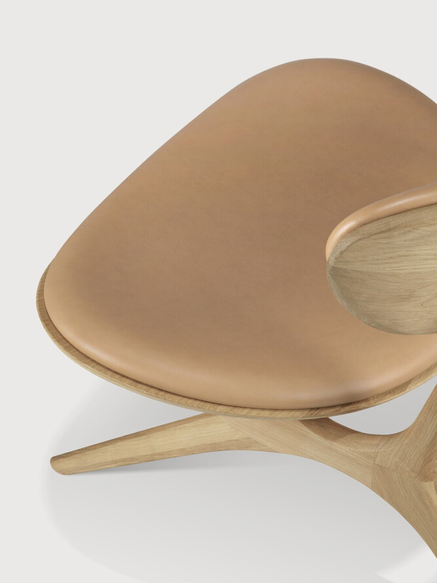 Ethnicraft Eye Lounge Chair, an organic modern lounge chair showcasing a sculptural light oak wood frame with fluid, curved lines and a seamlessly integrated armrest. It features a plush, rounded tan leather upholstered seat, offering sophisticated comfort and contemporary style. This designer accent chair is ideal for adding a minimalist touch to a living room, bedroom, or cozy reading nook.