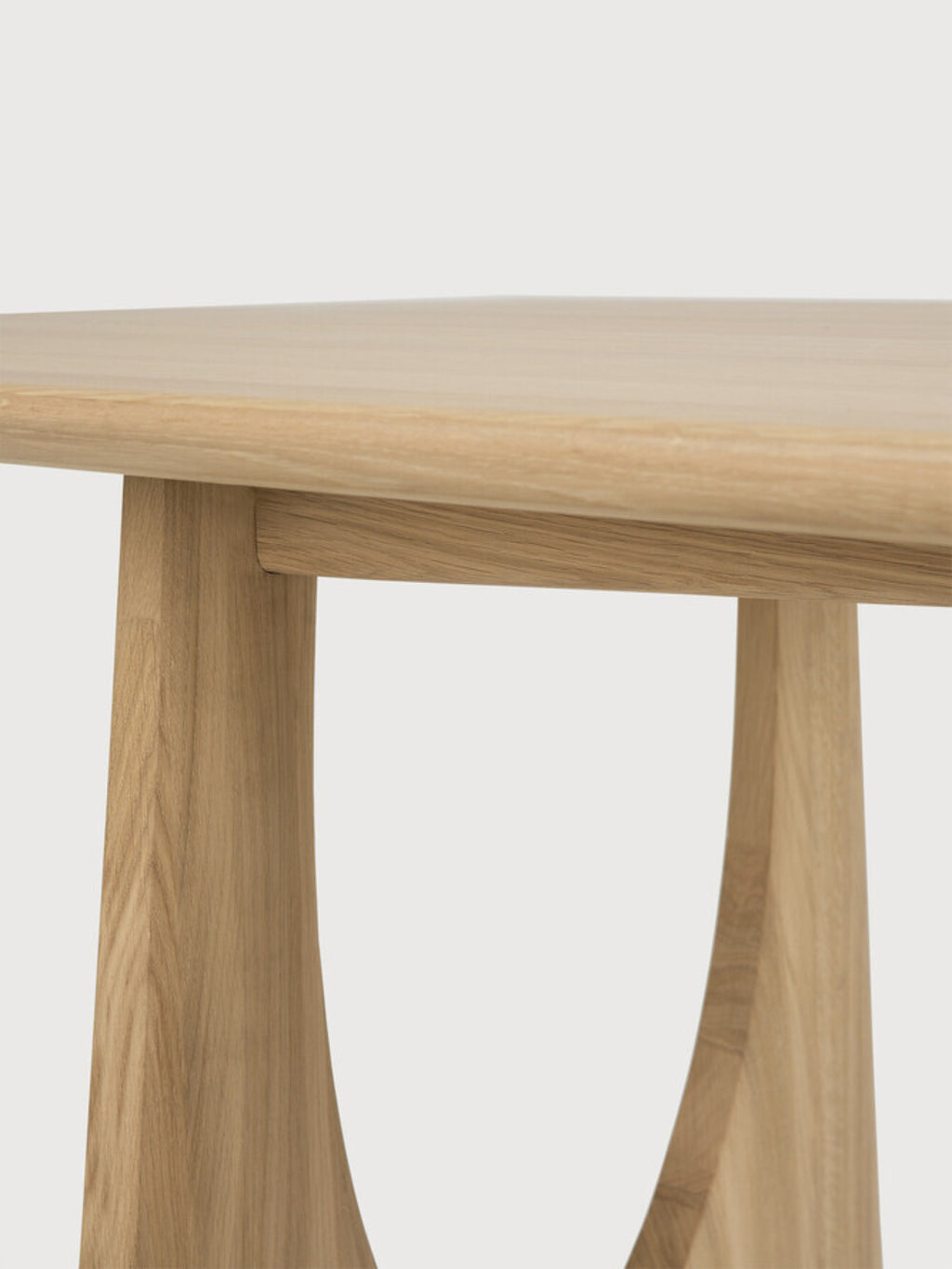 Ethnicraft Geometric Dining Table, a modern minimalist dining table crafted from smooth solid oak in a light natural finish, featuring a clean tabletop edge and distinctive sculptural, curved solid wood legs.