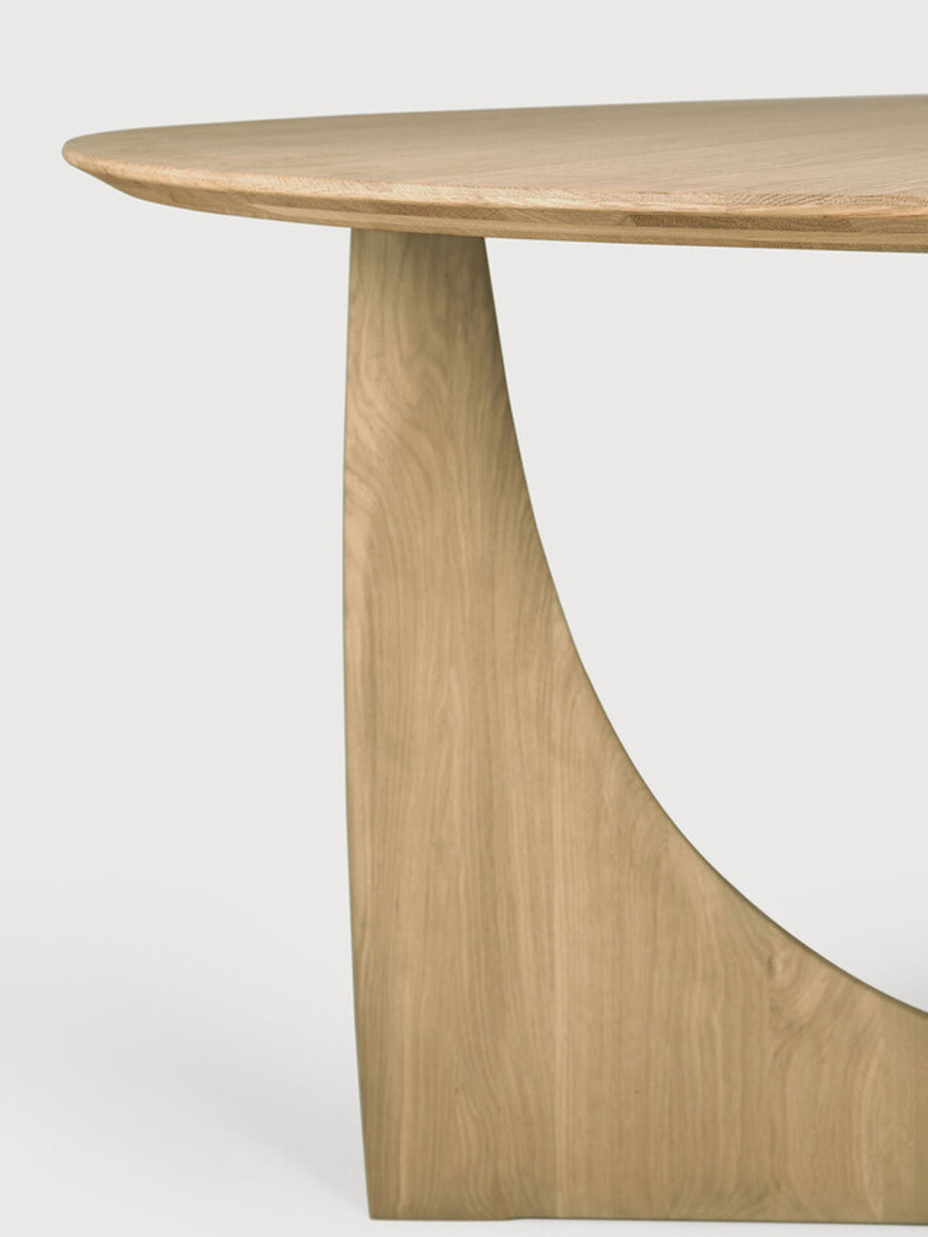 Ethnicraft Geometric Dining Table, a contemporary round dining table crafted from light natural solid oak with a smooth, visible wood grain. It features a distinctive sculptural pedestal base with an organic, curved geometric design, embodying an organic modern aesthetic. Ideal for minimalist dining rooms or open-plan living spaces seeking a statement piece.