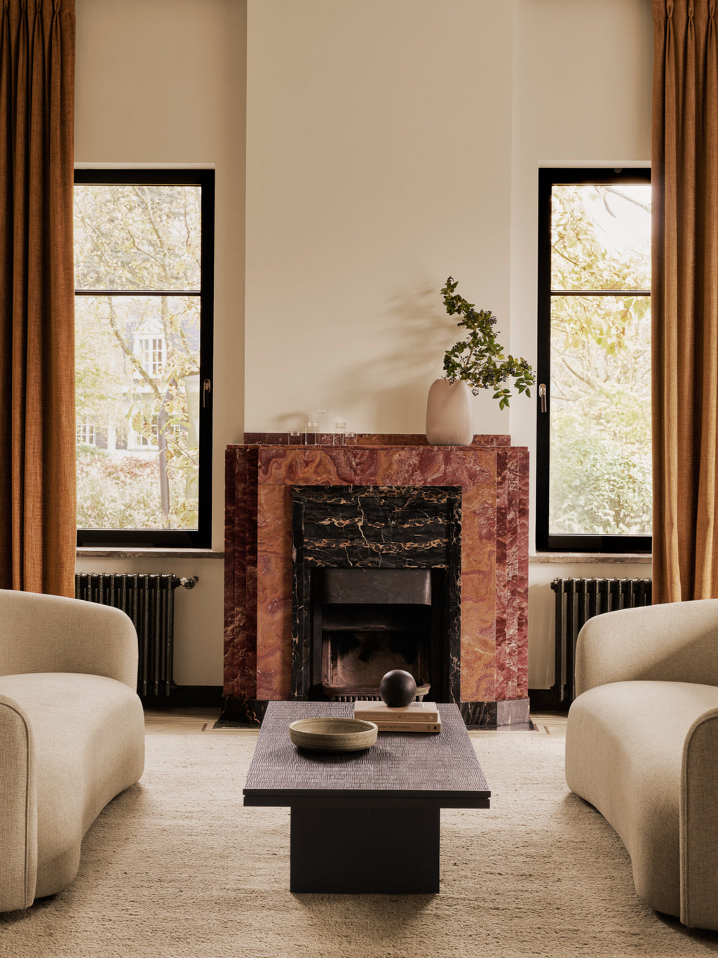 Ethnicraft Grooves Coffee Table, a striking off-black teak table with intricate carved patterns, centrally placed in an elegant living room with two beige armchairs and a fireplace.