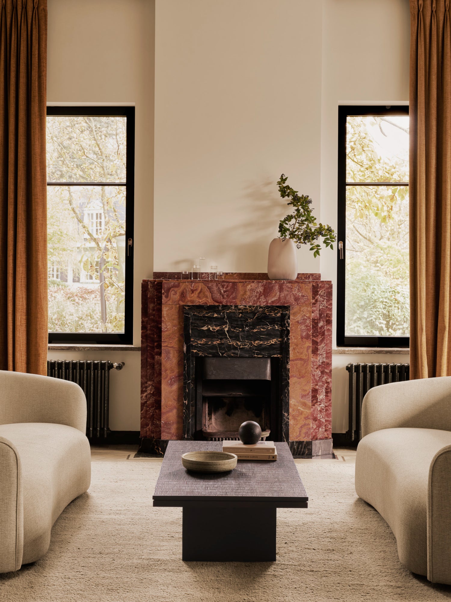 Ethnicraft Grooves Coffee Table, a striking off-black teak table with intricate carved patterns, centrally placed in an elegant living room with two beige armchairs and a fireplace.