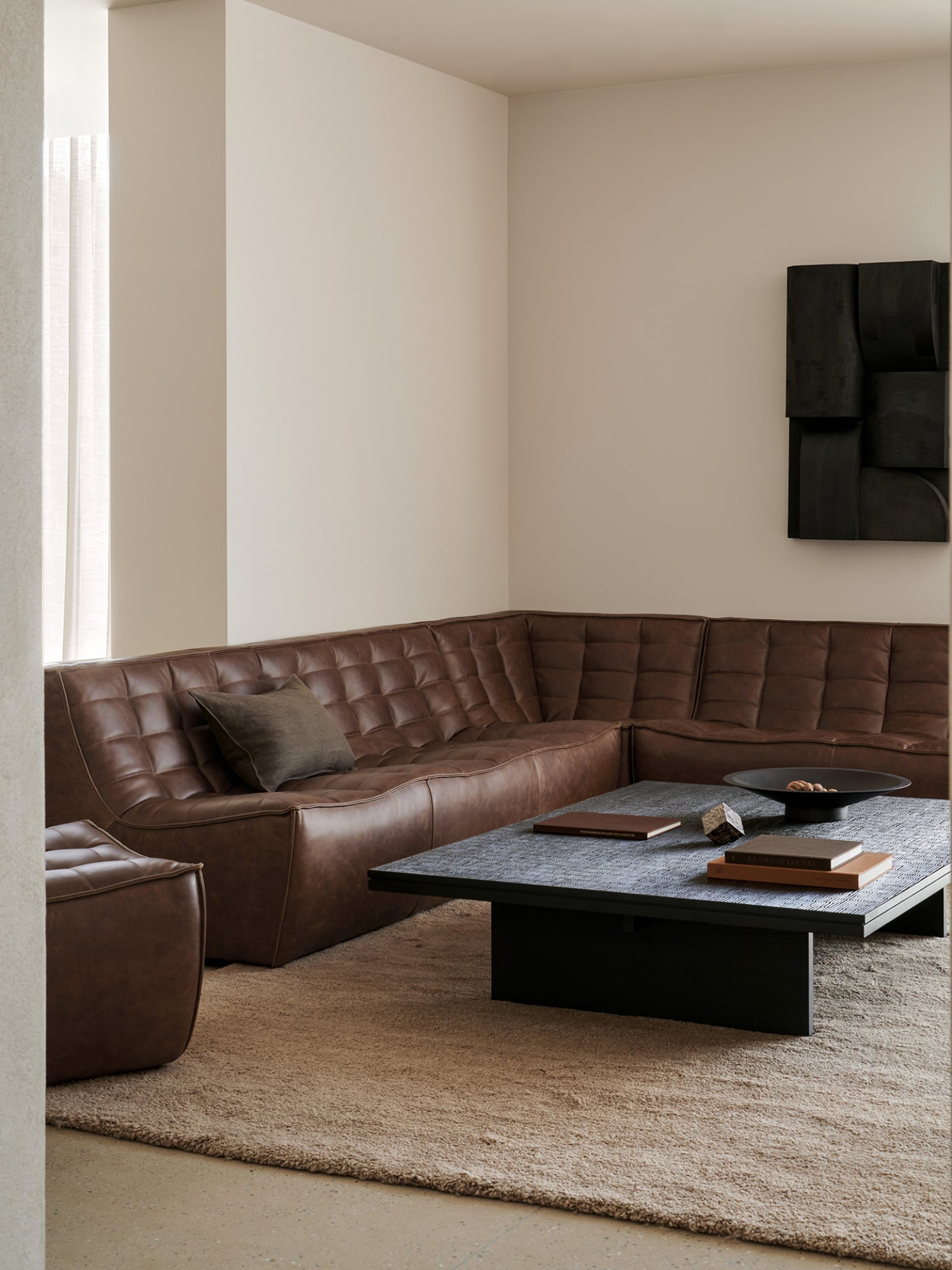 Ethnicraft Grooves Coffee Table, a sophisticated off-black teak table with a unique textured surface, styled in a modern living room with a brown leather sofa and neutral rug.