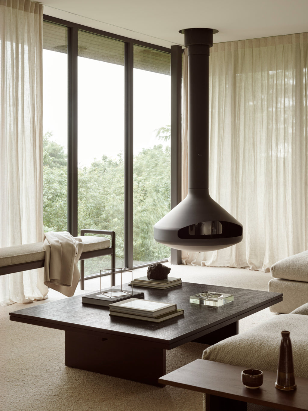 Ethnicraft Grooves Coffee Table, a large, rectangular off-black teak table with a textured top, anchoring a luxurious living space with a suspended fireplace and floor-to-ceiling windows.