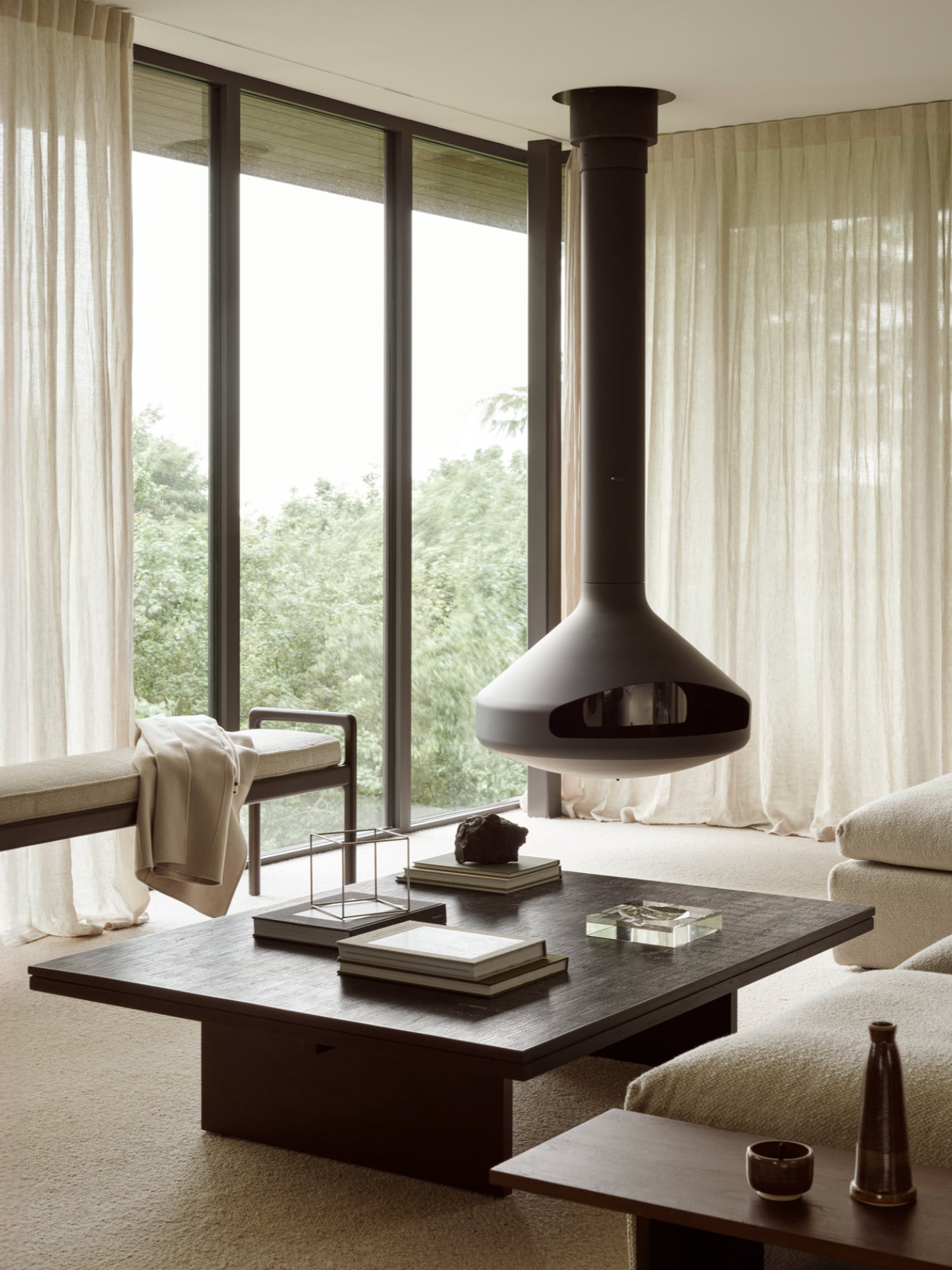 Ethnicraft Grooves Coffee Table, a large, rectangular off-black teak table with a textured top, anchoring a luxurious living space with a suspended fireplace and floor-to-ceiling windows.