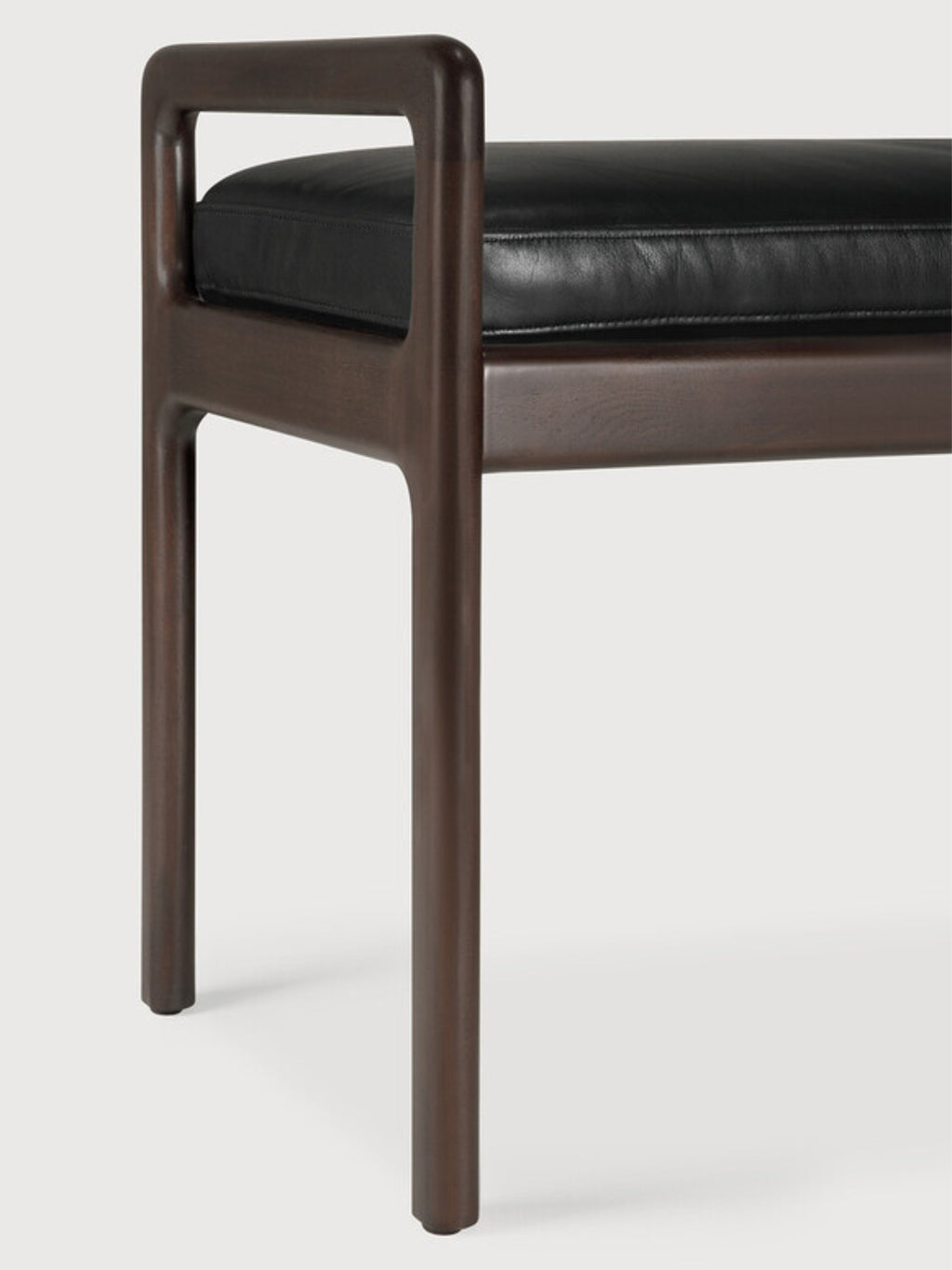 Ethnicraft Jack Bench, a close-up detail of the sturdy mahogany dark brown wooden leg and armrest, paired with the smooth black leather cushion, on a clean white background.
