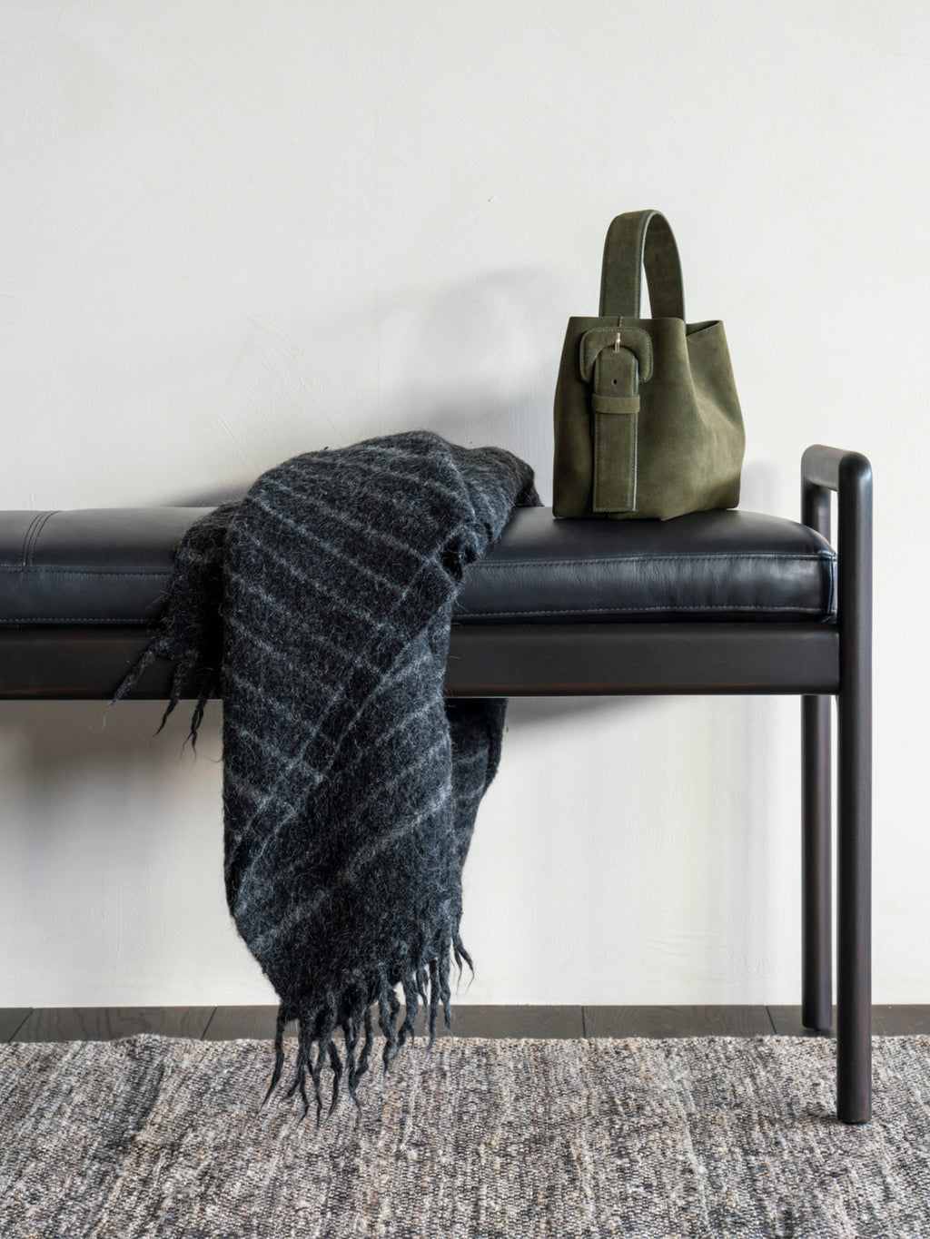 Ethnicraft Jack Bench in mahogany dark brown with a premium black leather cushion, styled with a dark gray patterned throw blanket and a green handbag in a modern interior.
