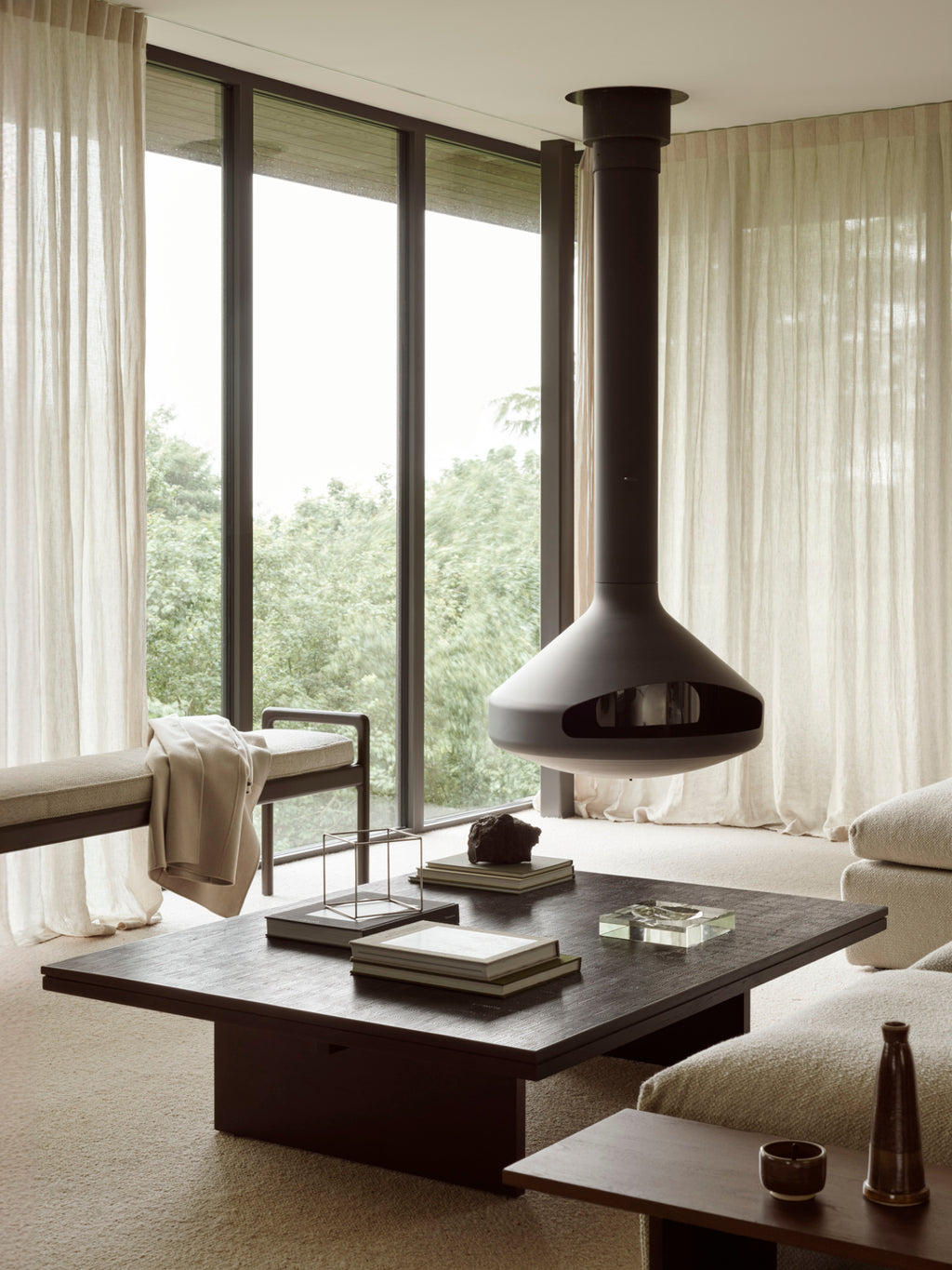 Ethnicraft Jack Bench in mahogany dark brown with an ivory cushion, placed in a luxurious living room setting with large windows, a hanging fireplace, and light curtains.