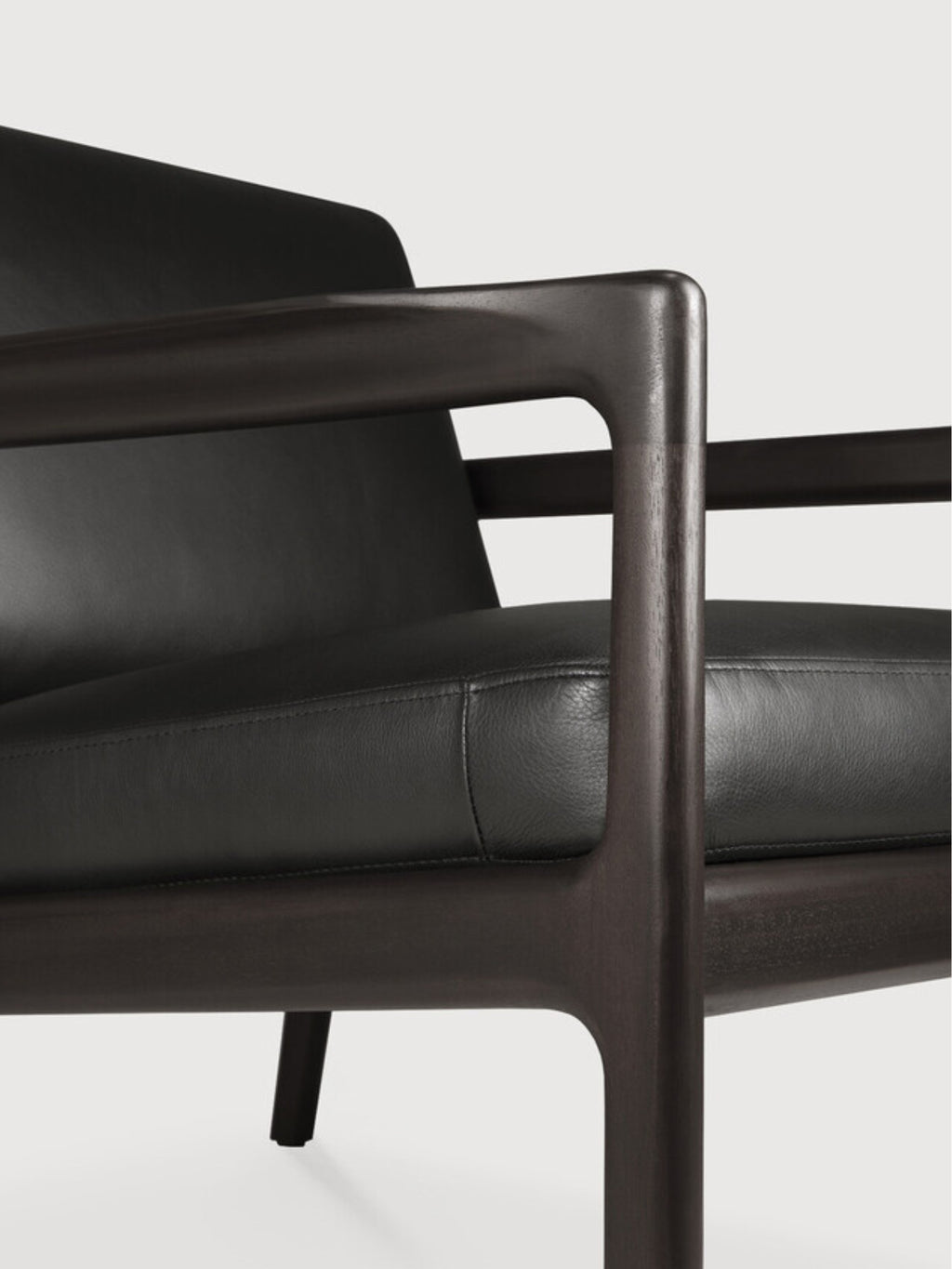Ethnicraft Jack Lounge Chair, a sophisticated modern lounge chair featuring a dark solid wood frame with smoothly rounded edges and a low-profile silhouette, complemented by plush matte black leather cushions with subtle stitching details.