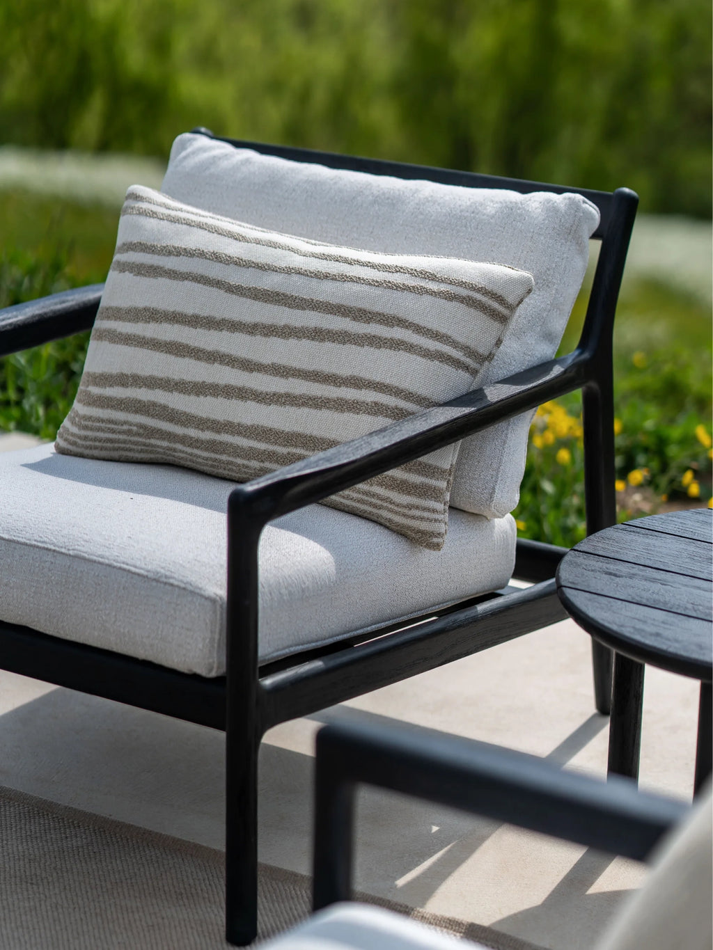 Ethnicraft Jack Lounge Chair, a sleek modern lounge chair featuring a sturdy black stained solid teak wood frame with clean lines and plush light grey upholstered outdoor cushions. It includes a decorative accent pillow with textured beige striped patterns on an off-white base, ideal for creating a minimalist and comfortable setting on a contemporary patio, garden, or deck.